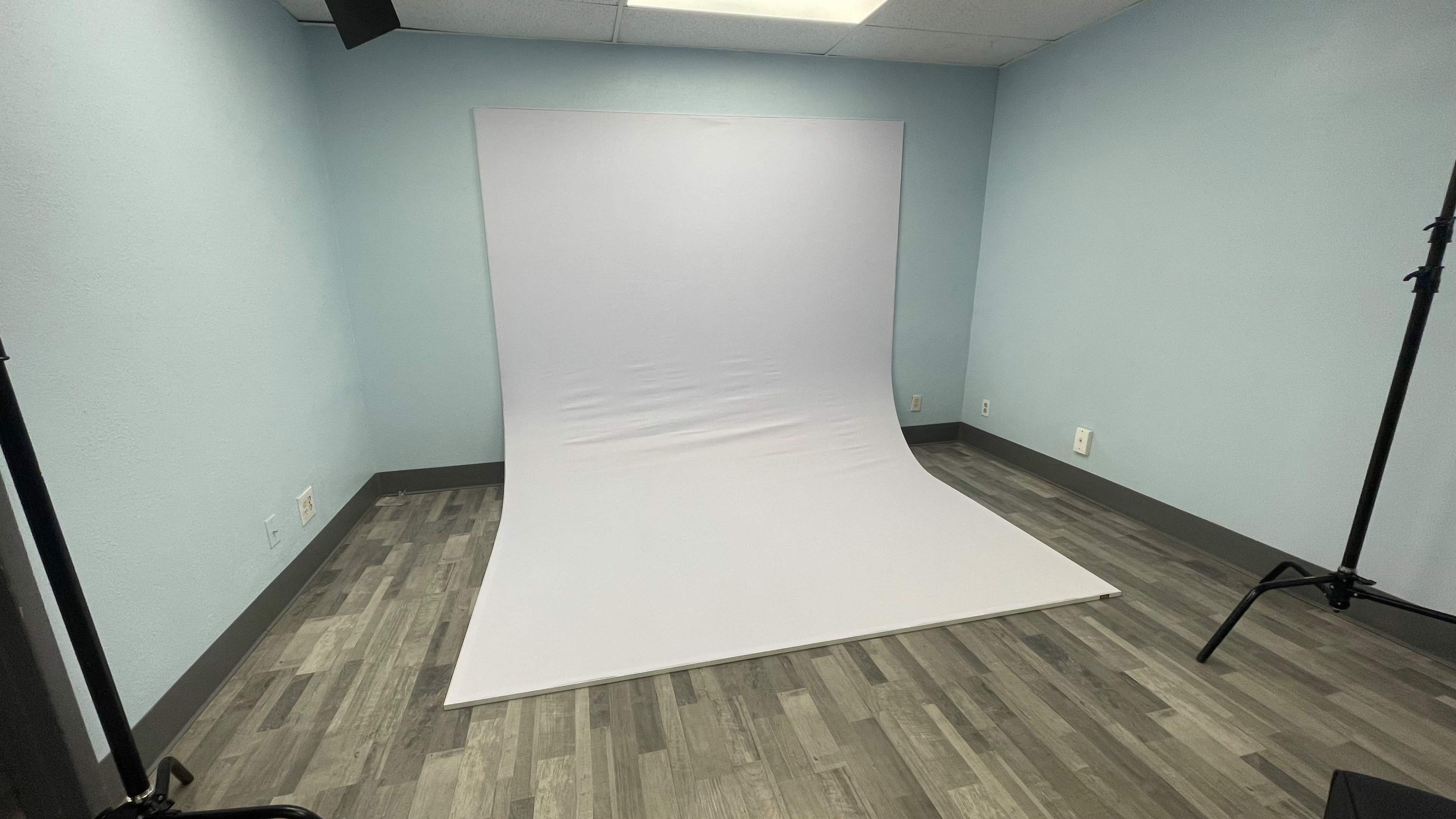 A blank photography studio with a white backdrop set against light blue walls and a wooden floor.