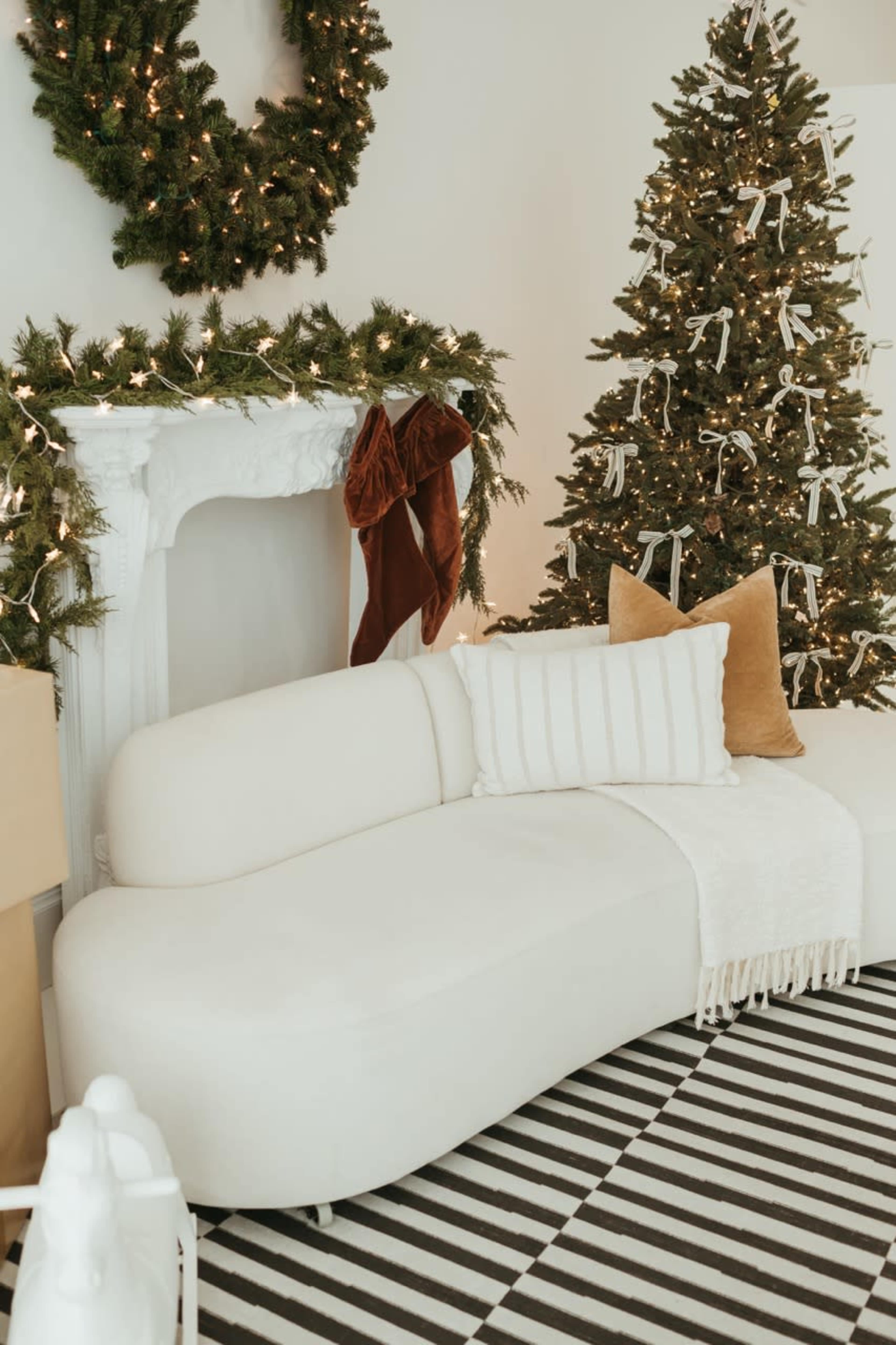 The image features a cozy living room with a white curved sofa, a decorated Christmas tree, and a fireplace adorned with greenery and lights.