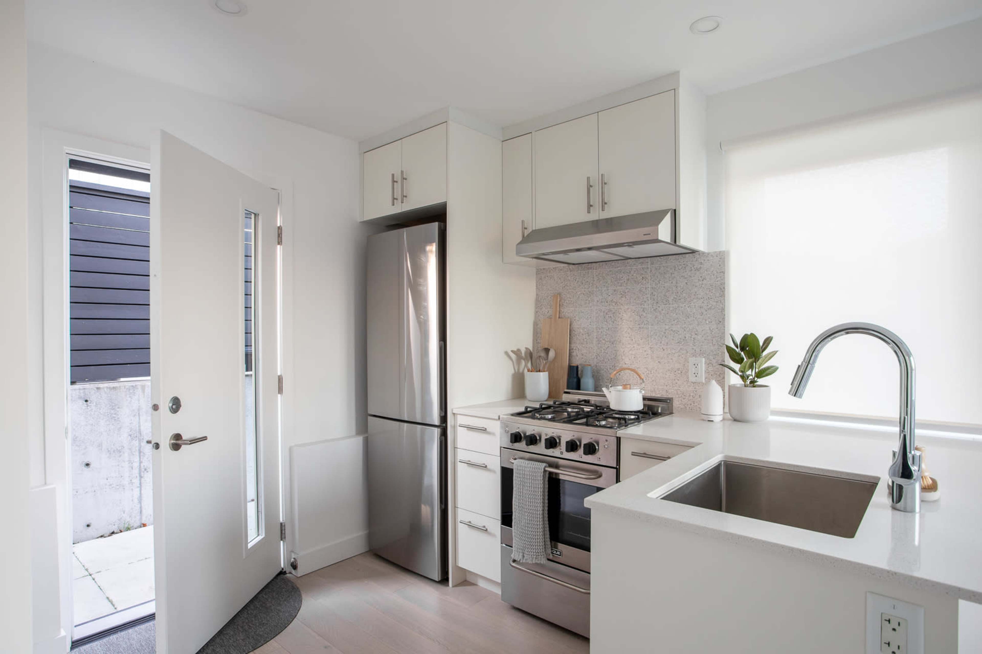 A modern kitchen features stainless steel appliances, white cabinetry, and a door leading to an outdoor area.