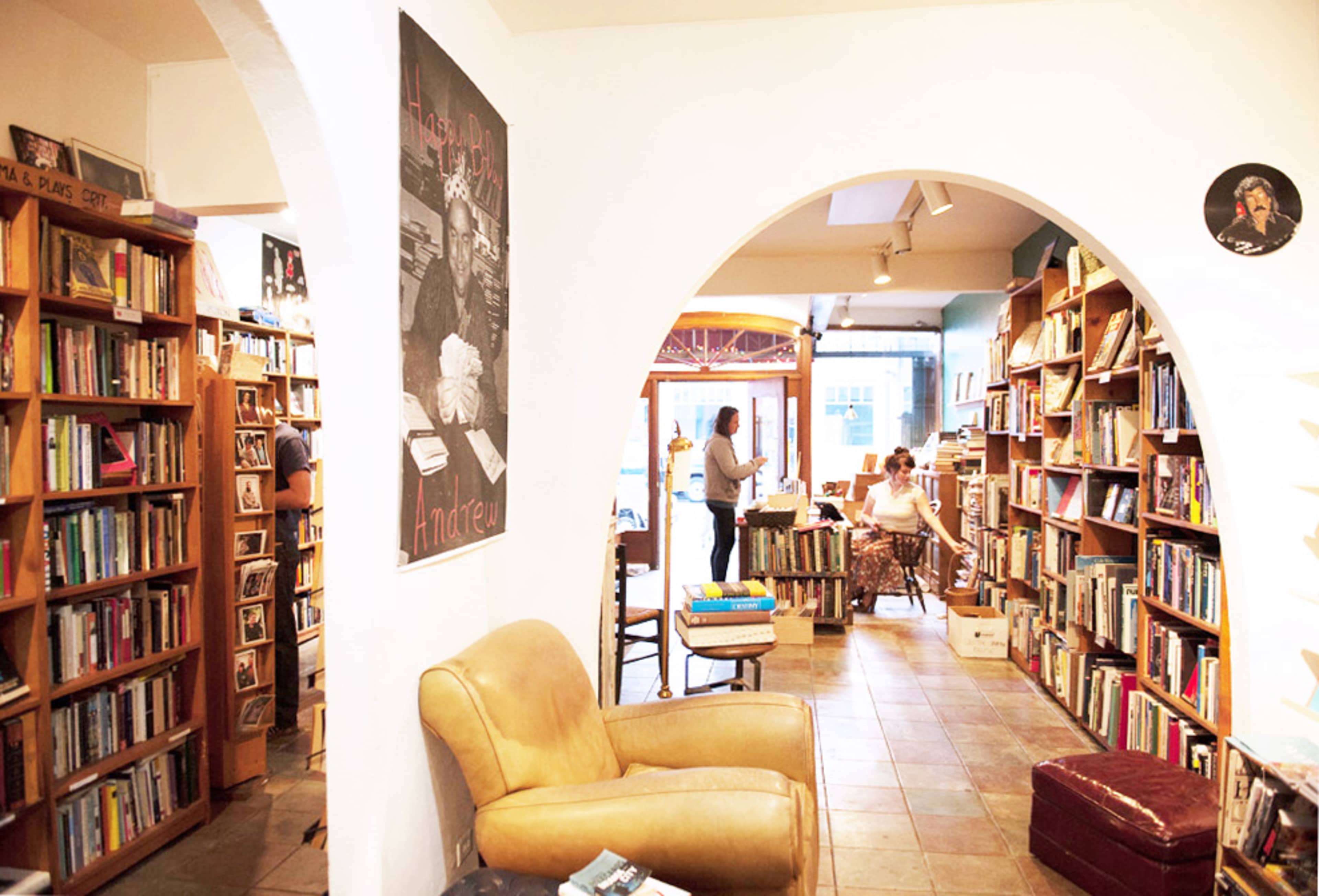 A cozy bookstore with wooden shelves filled with books, arches leading into different areas, and a couple of people browsing and reading.