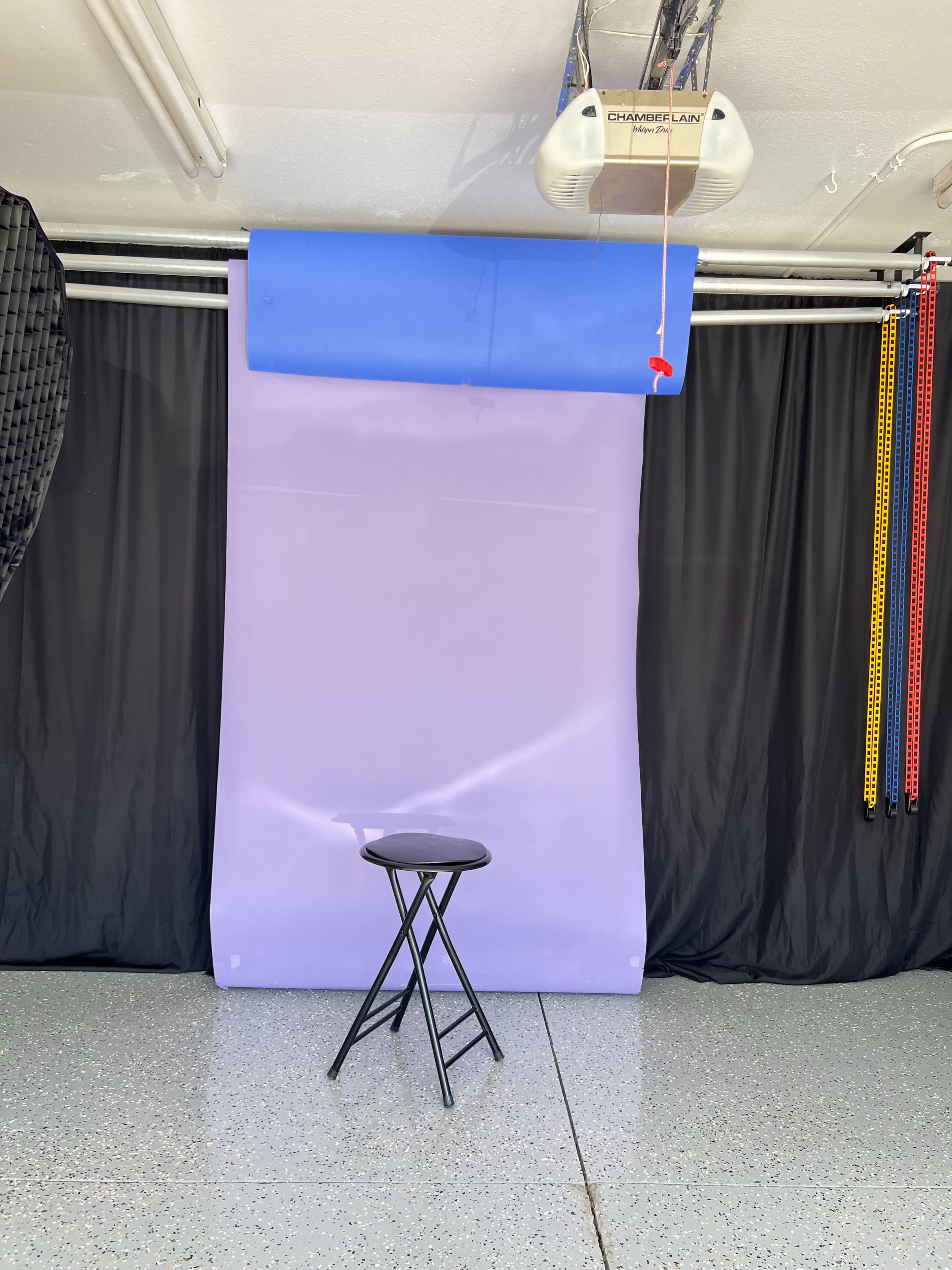 A photography setup featuring a purple backdrop, a black stool, and black curtains in a garage space.