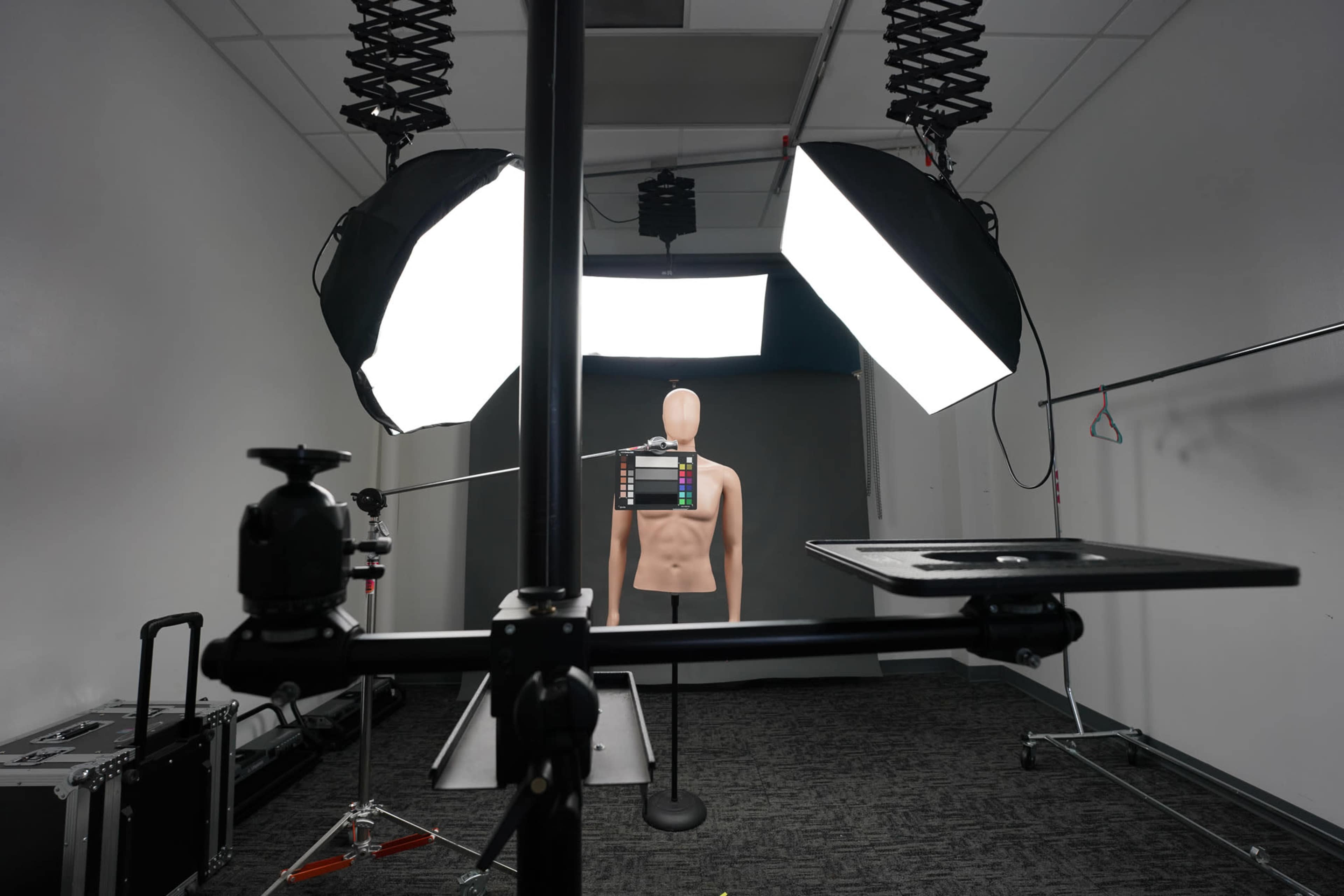 The image shows a photography studio set up with softbox lights, a mannequin positioned at the center, and various equipment including a camera mount and backdrop.