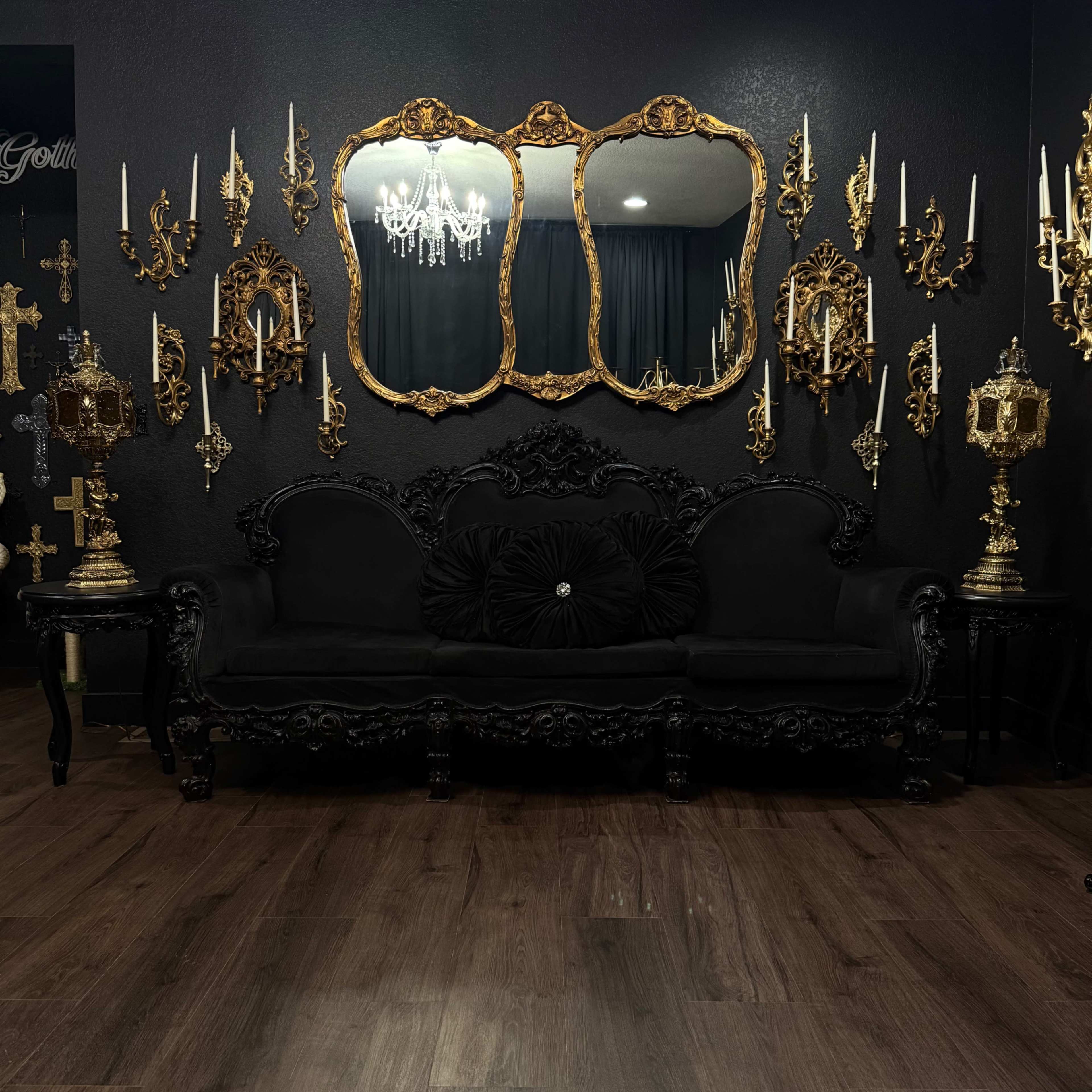 The image shows a black ornate couch against a wall adorned with intricate gold mirrors and wall sconces.