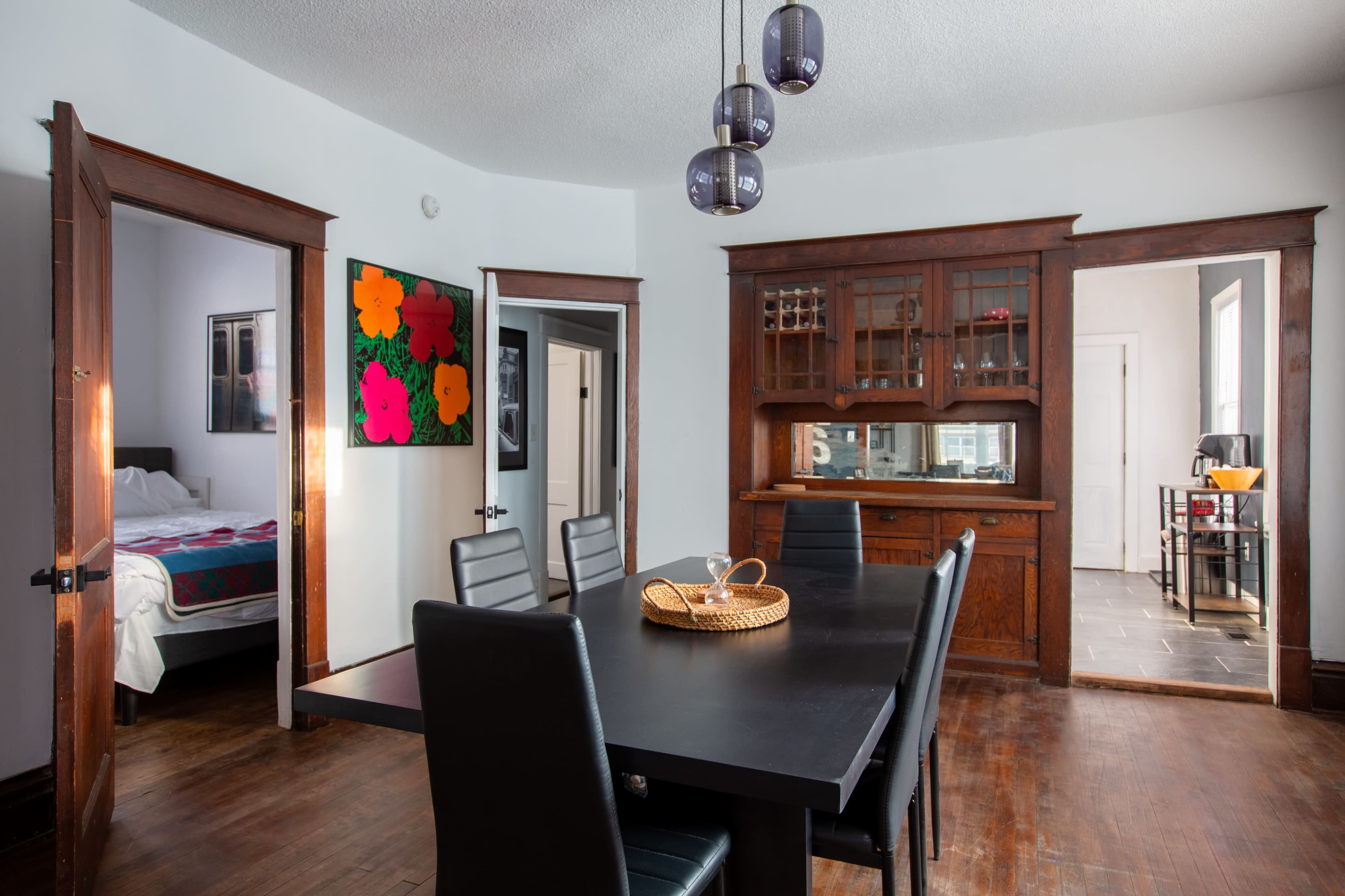 A dining room features a large black table surrounded by chairs, with doors leading to an adjacent room and a sideboard against the wall.