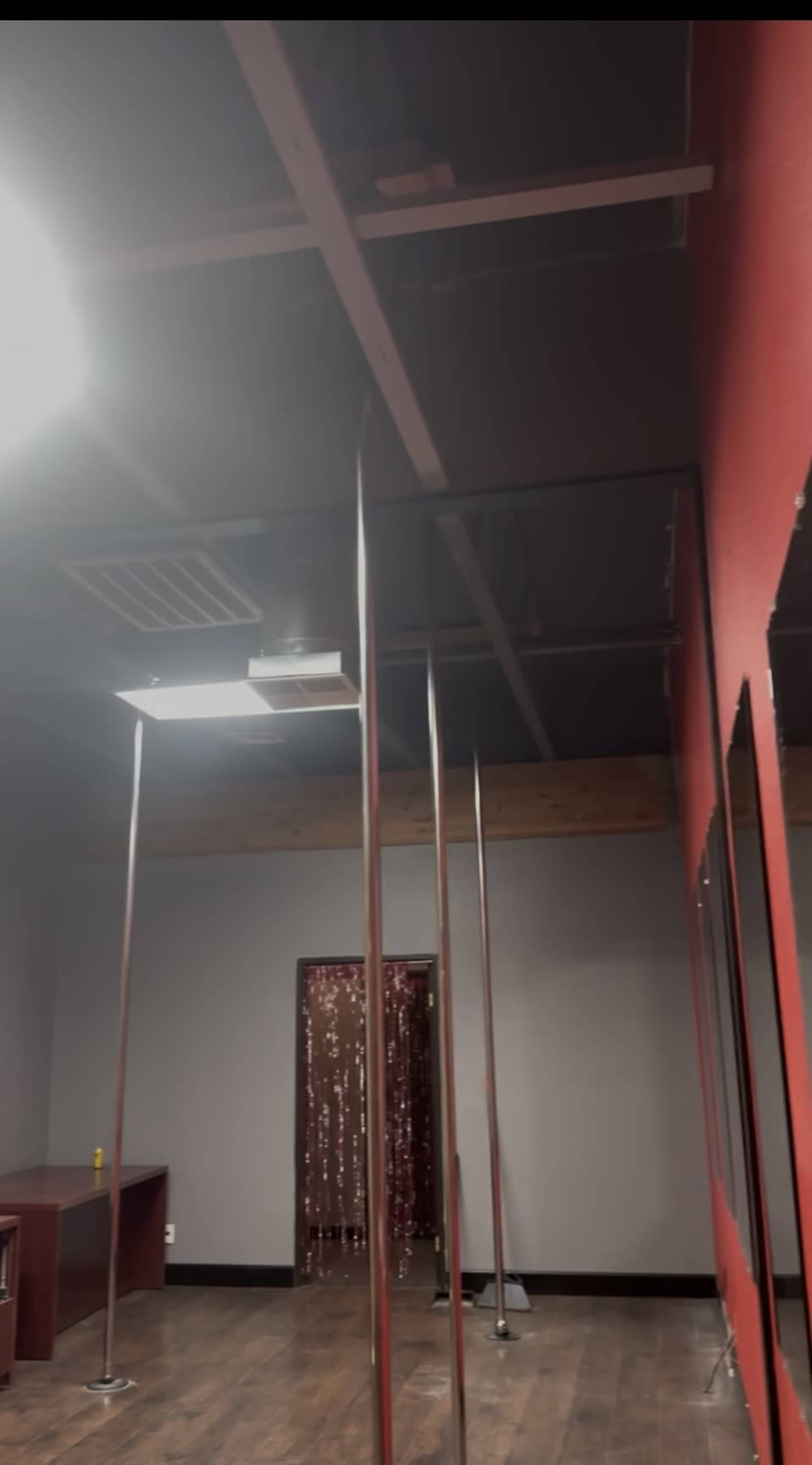 The image shows an interior space with several vertical poles, a wooden floor, and a backdrop of shimmering decorations in a doorway.