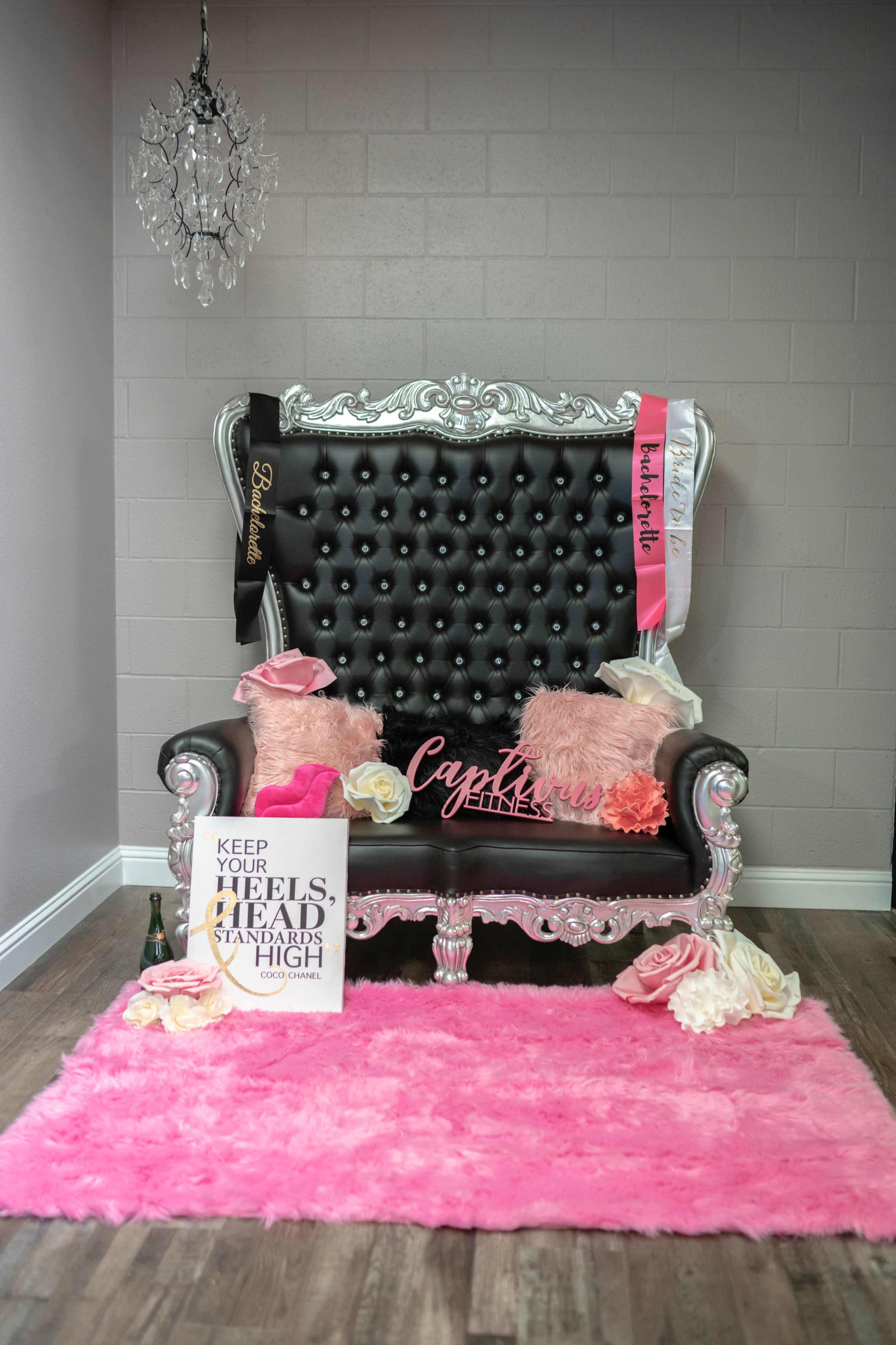 An ornate black and silver chair adorned with plush pink decorations and a motivational poster on a wall with a light fixture above.