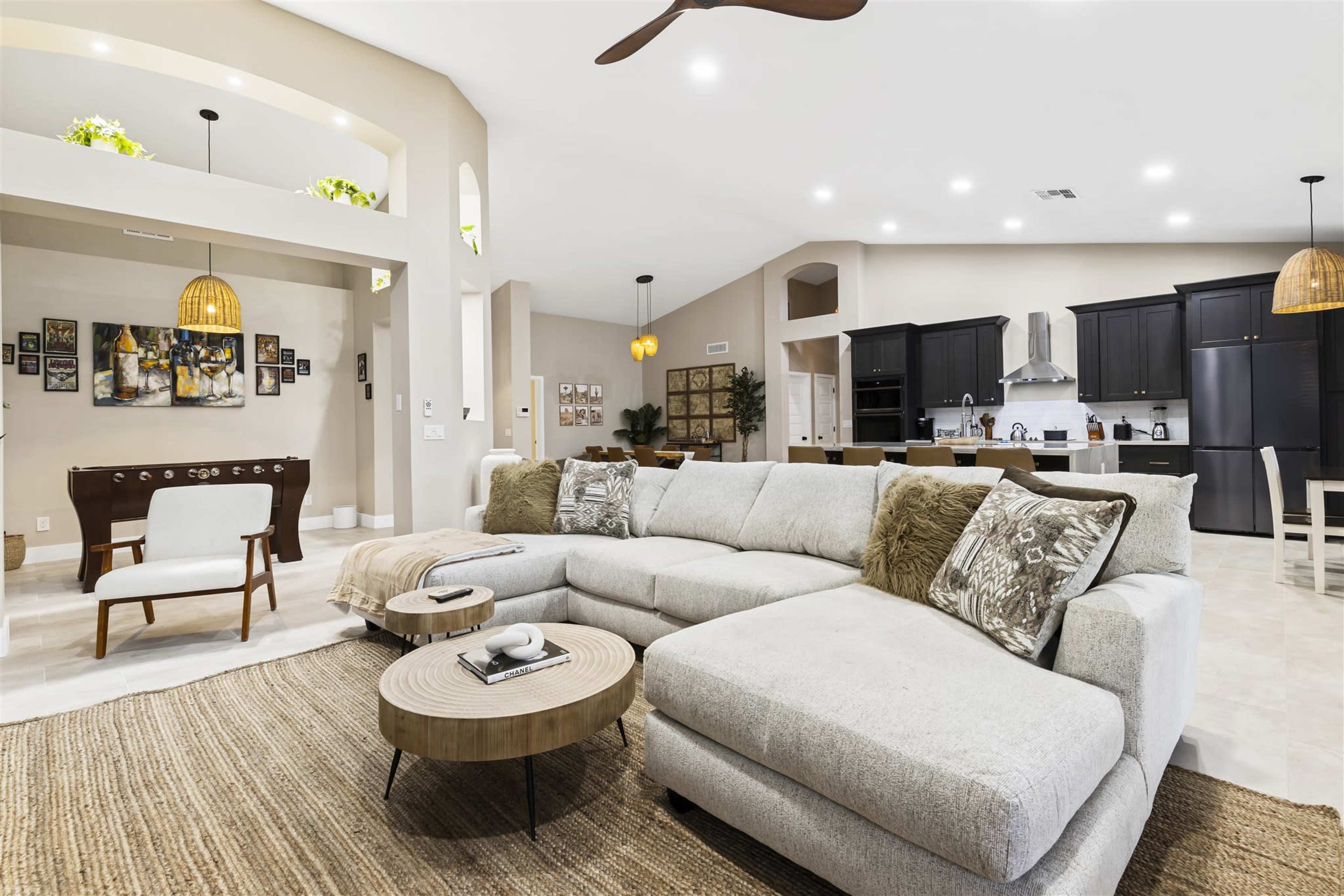 A spacious living area with a light-colored sectional sofa, a round coffee table, and a view of a modern kitchen in the background.