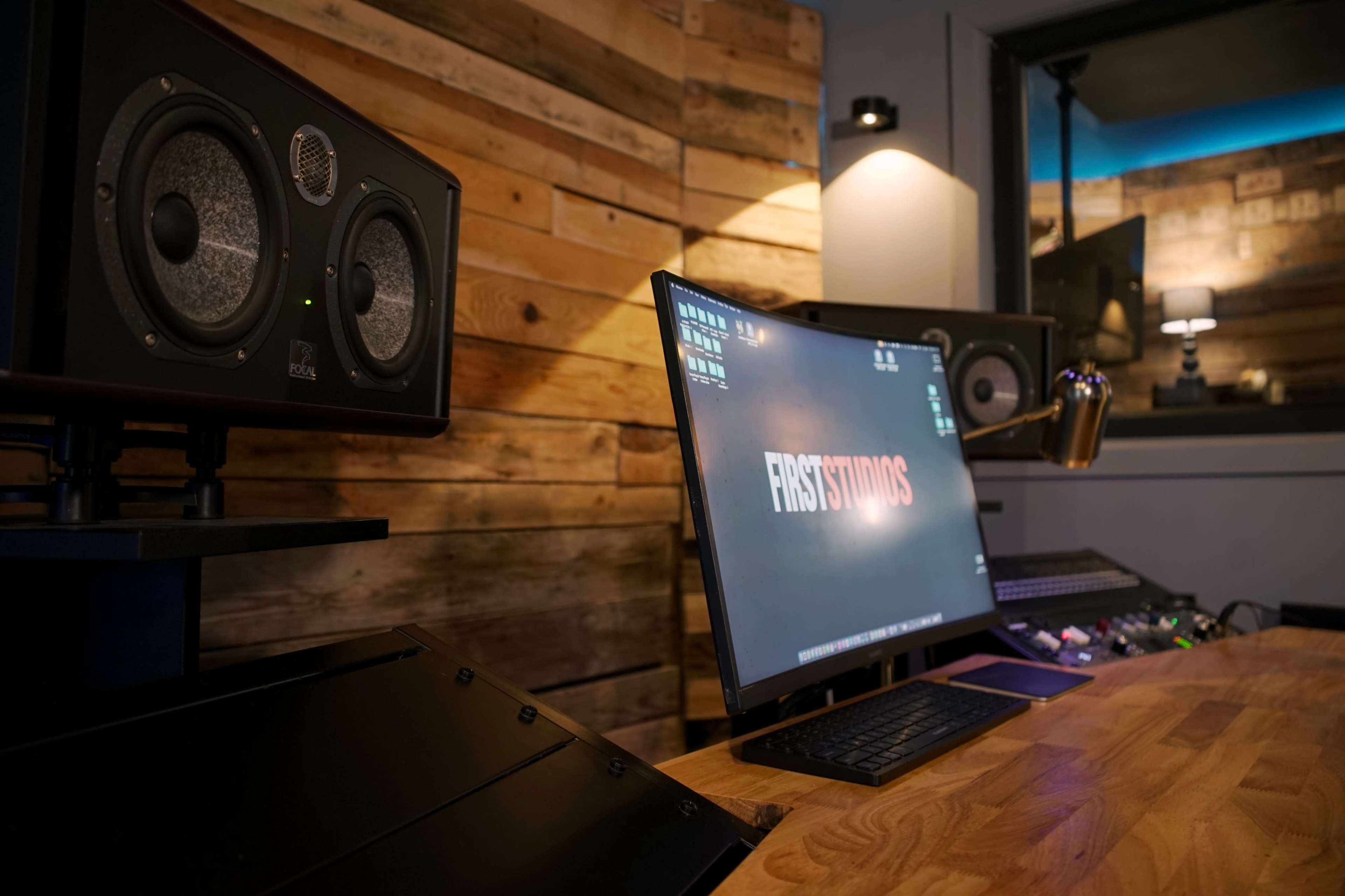 The image shows a modern recording studio with a wooden accent wall, featuring computer monitors, speakers, and audio equipment on a wooden desk.