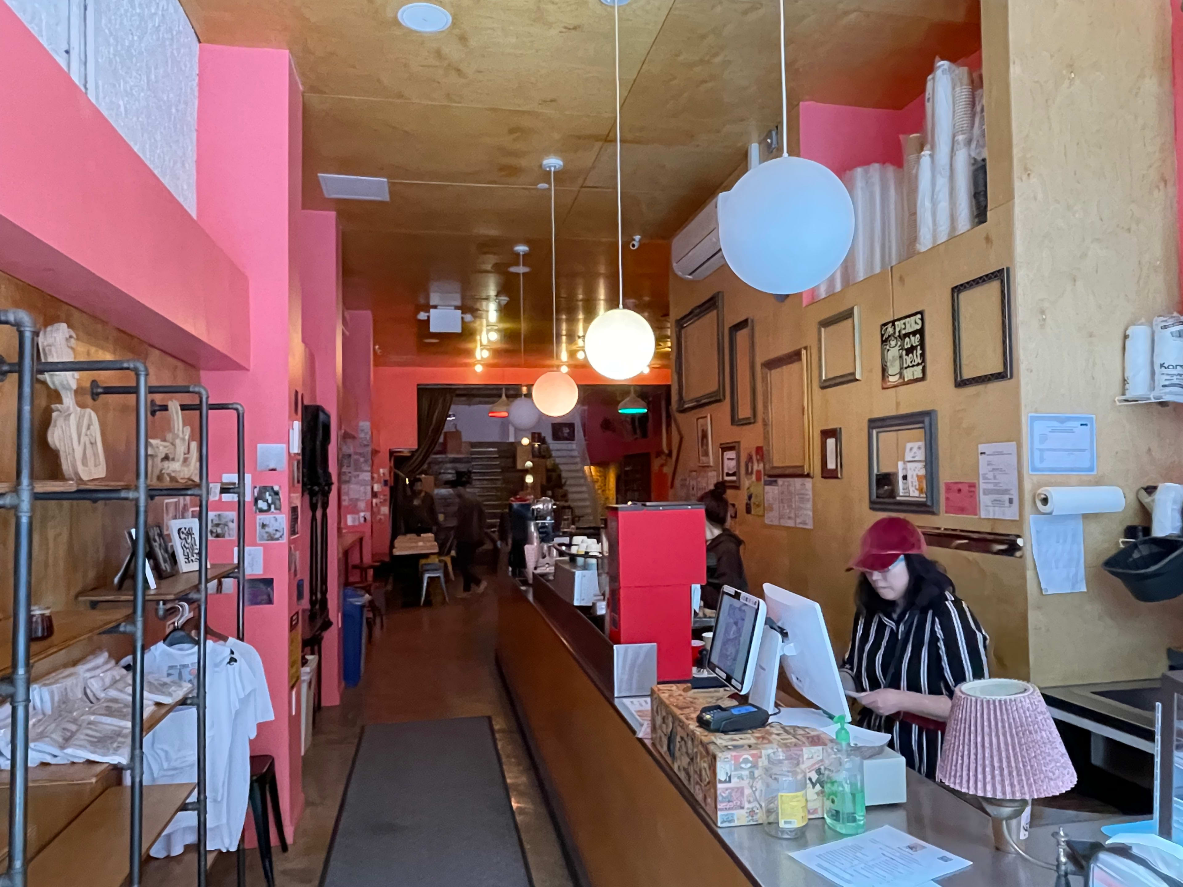 A brightly colored café interior with a long counter, overhead lighting, and a visible cashier attending to customers.