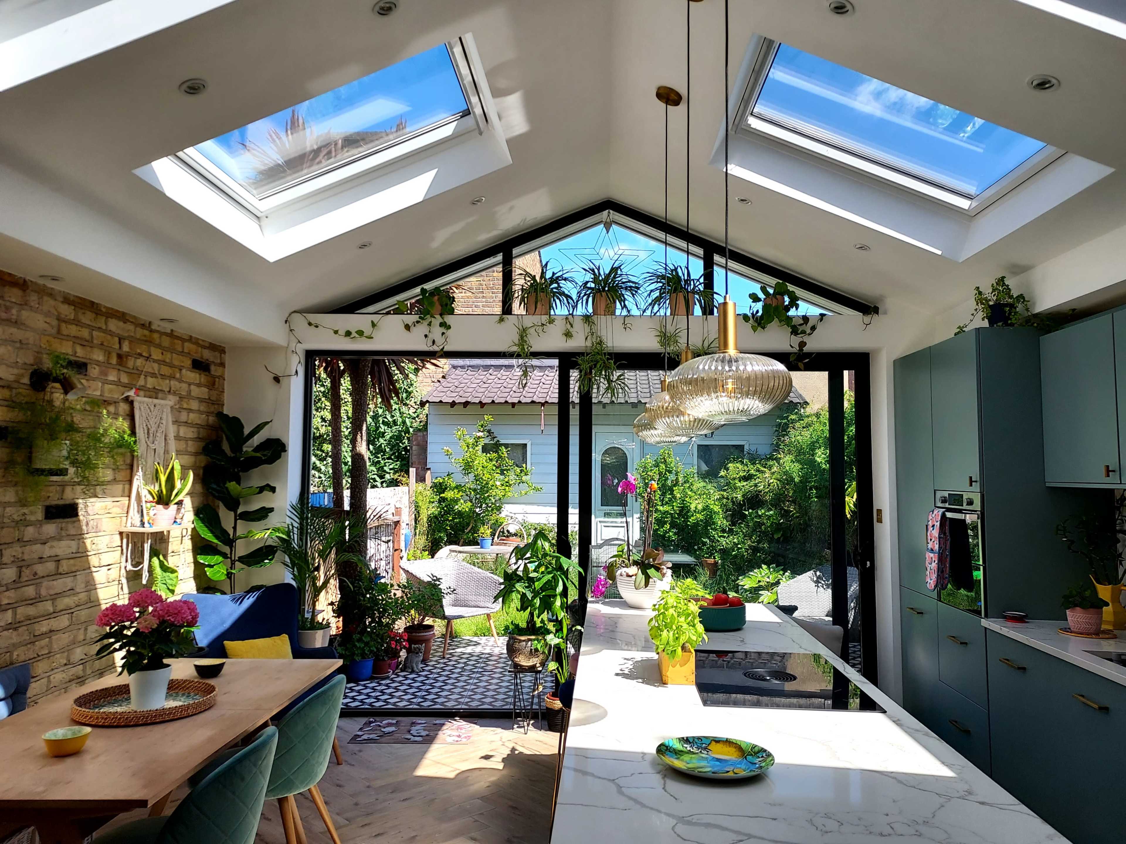 A bright kitchen with skylights, large glass doors opening to a garden, and various indoor plants adorning the space.