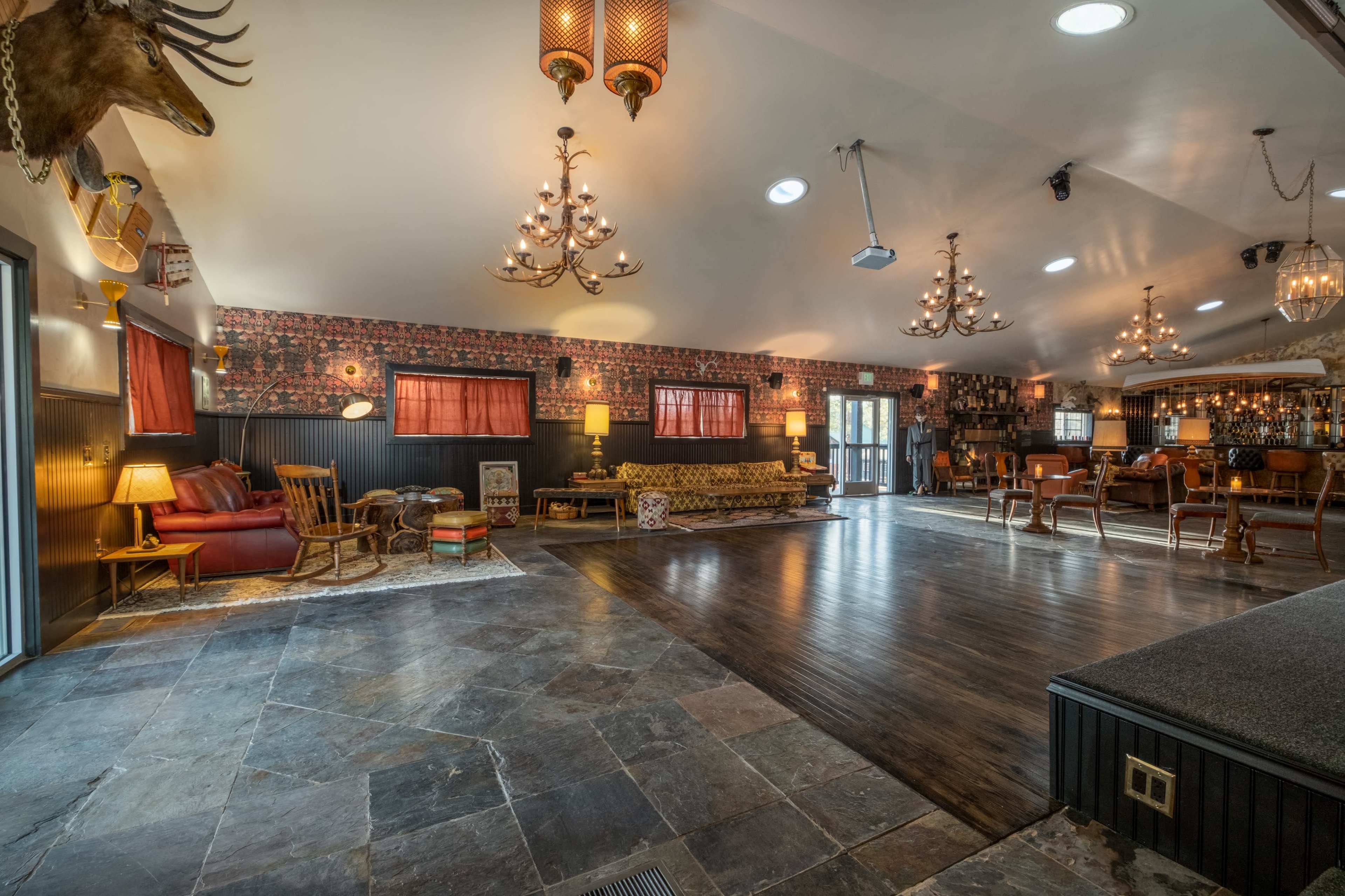 A spacious interior recreational room featuring a bar area, chandeliers, patterned wallpaper, and various seating arrangements.