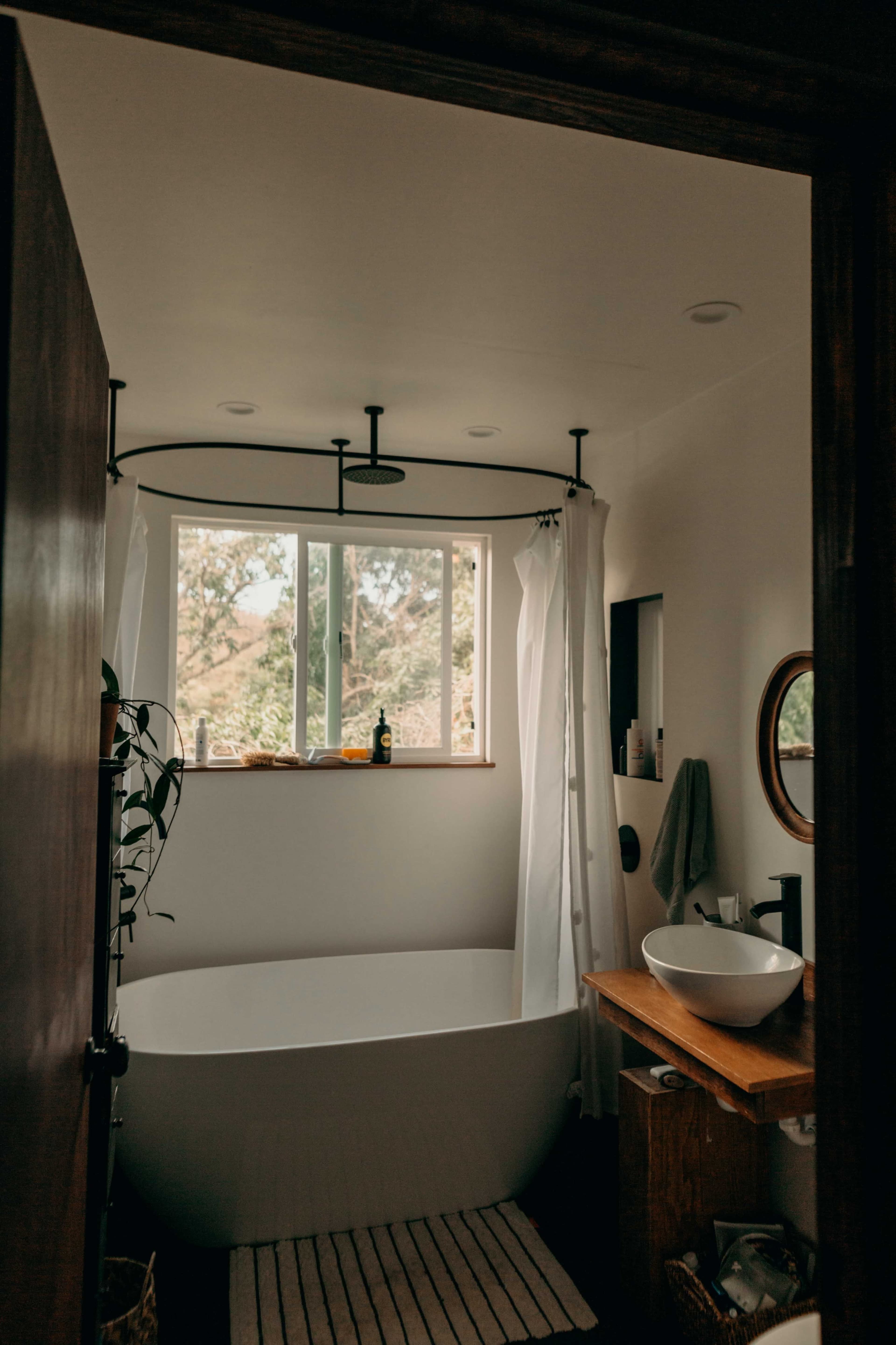 A bright bathroom featuring a freestanding bathtub, a window with views, and a wooden vanity.