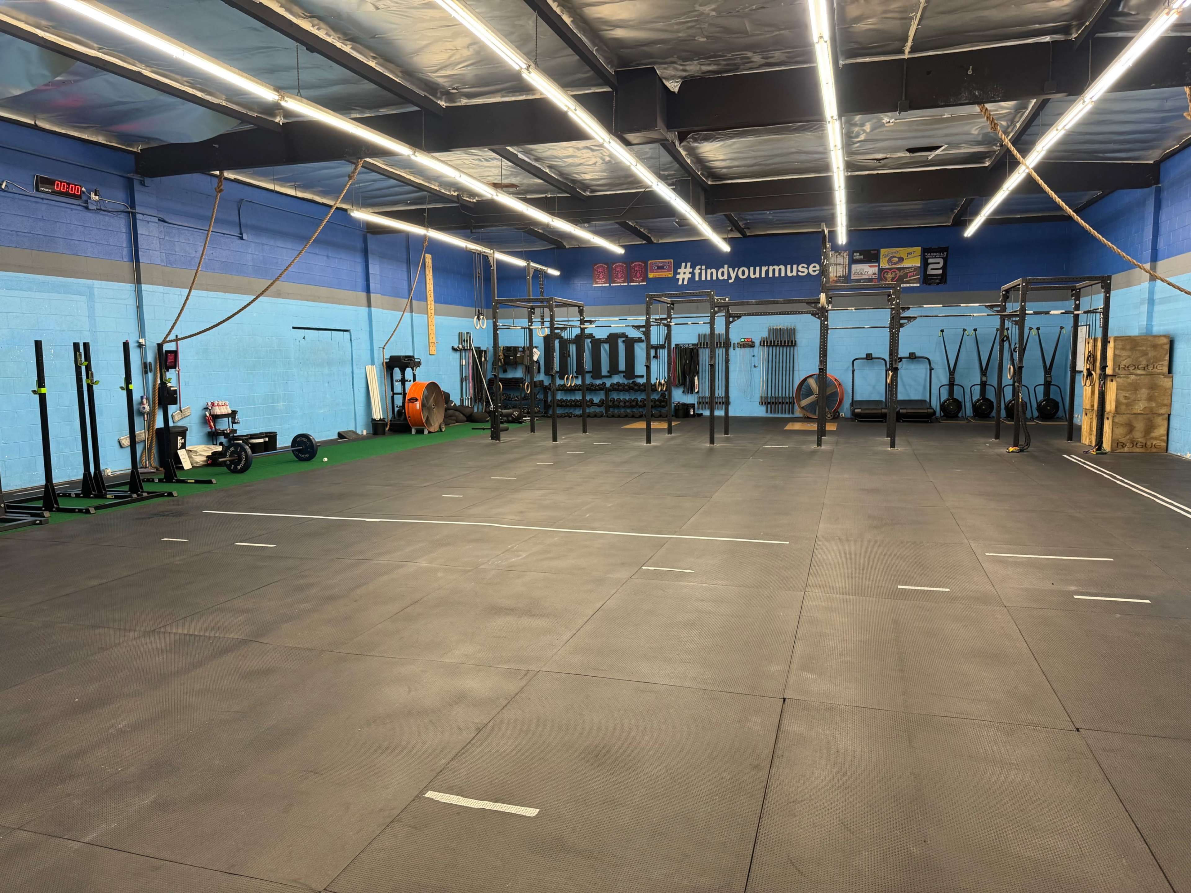 The image shows a fitness gym with various workout equipment, including weightlifting racks and exercise machines, set on a rubber flooring surface.