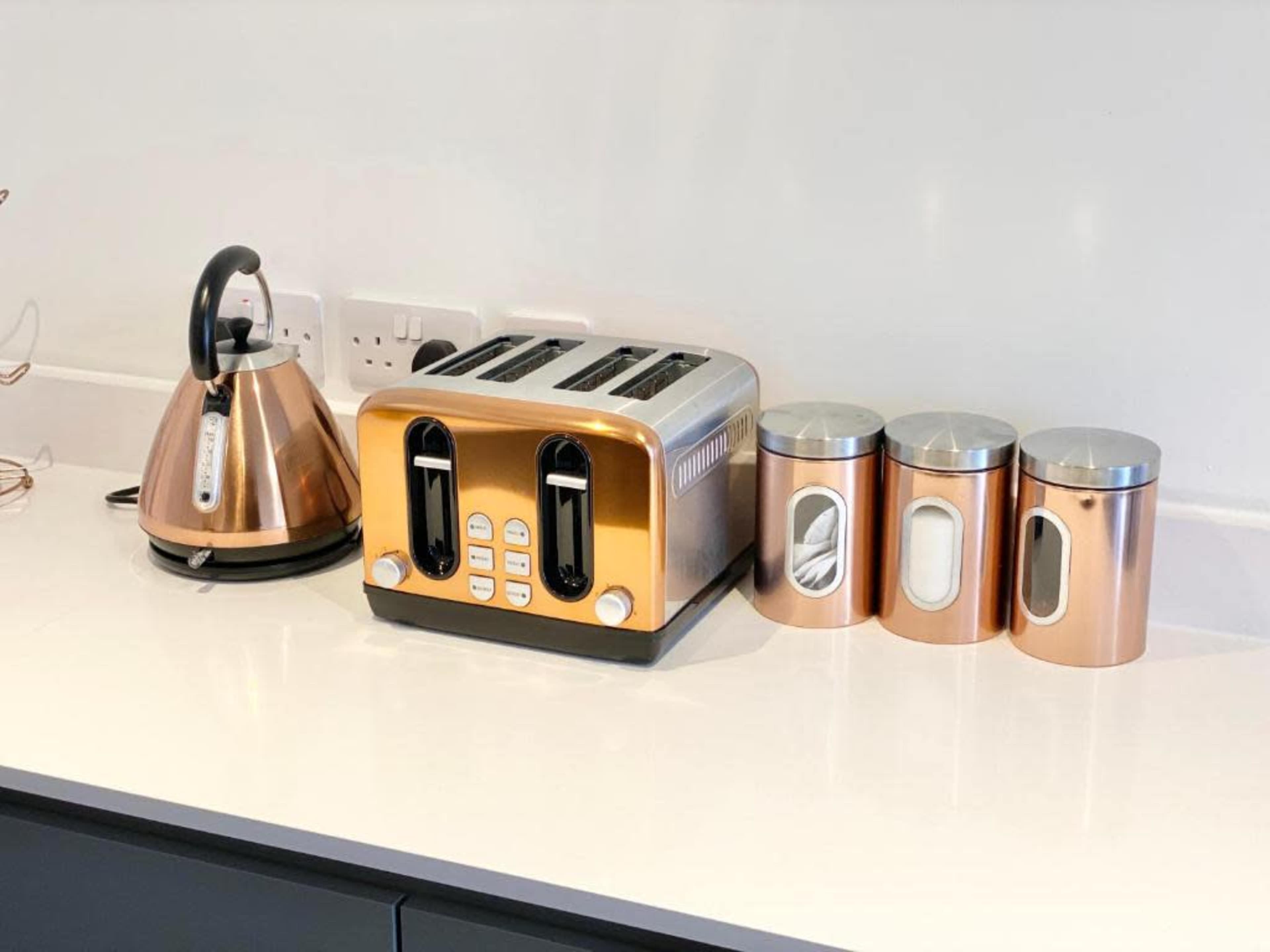 A copper-colored kettle and toaster sit on a white countertop alongside three matching storage canisters.
