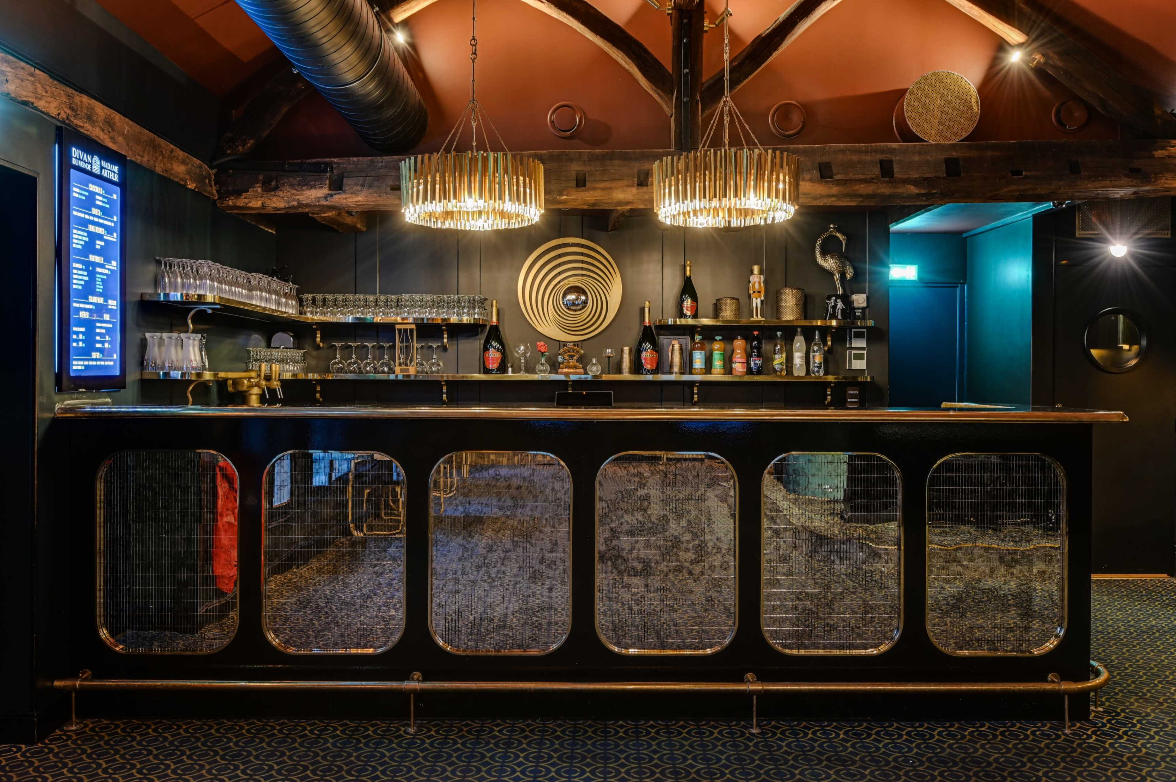 The image shows a modern bar area with a sleek counter, glassware on the shelves, and decorative lighting hanging above.