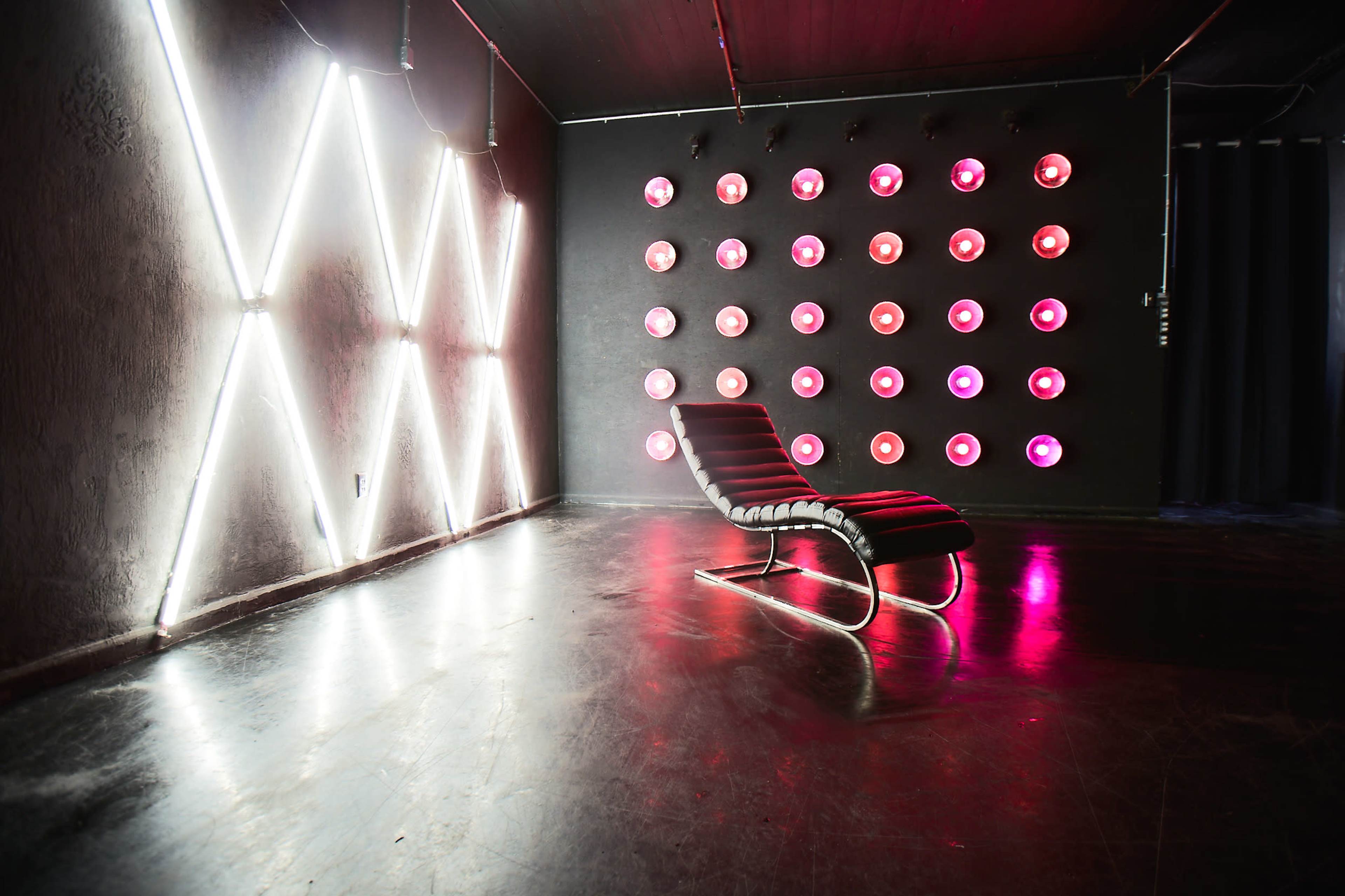 A sparse room featuring a striped lounge chair beside illuminated geometric neon patterns and a wall adorned with circular light fixtures.