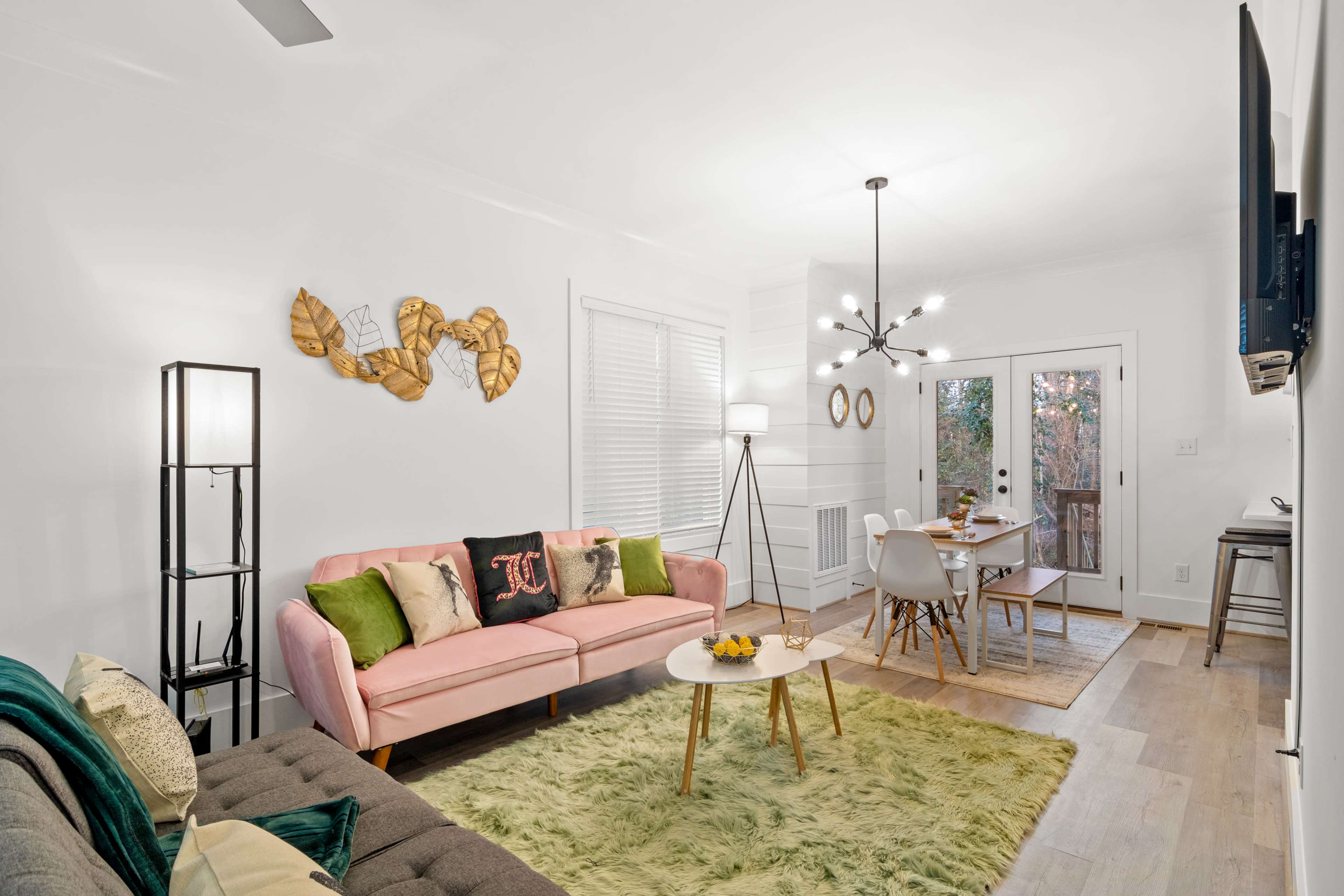 A cozy living area with a pink sofa, green and gray accents, a circular coffee table, and a dining area visible through sliding glass doors.