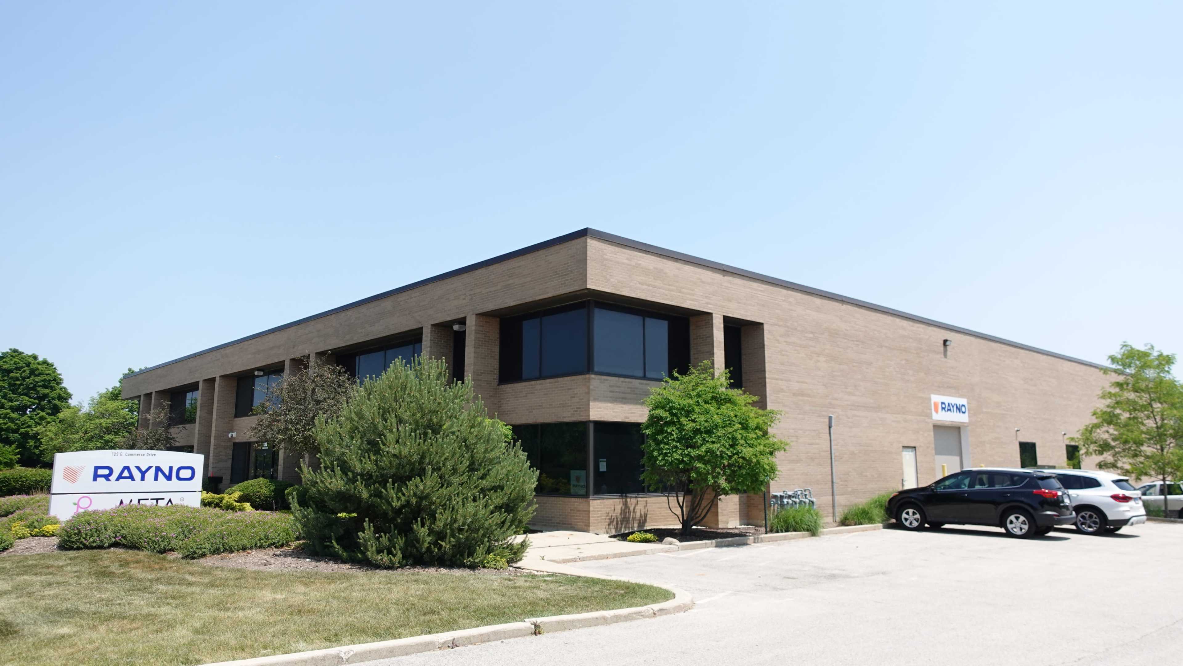A modern brick office building with large windows and a landscaped parking lot is shown in the image.
