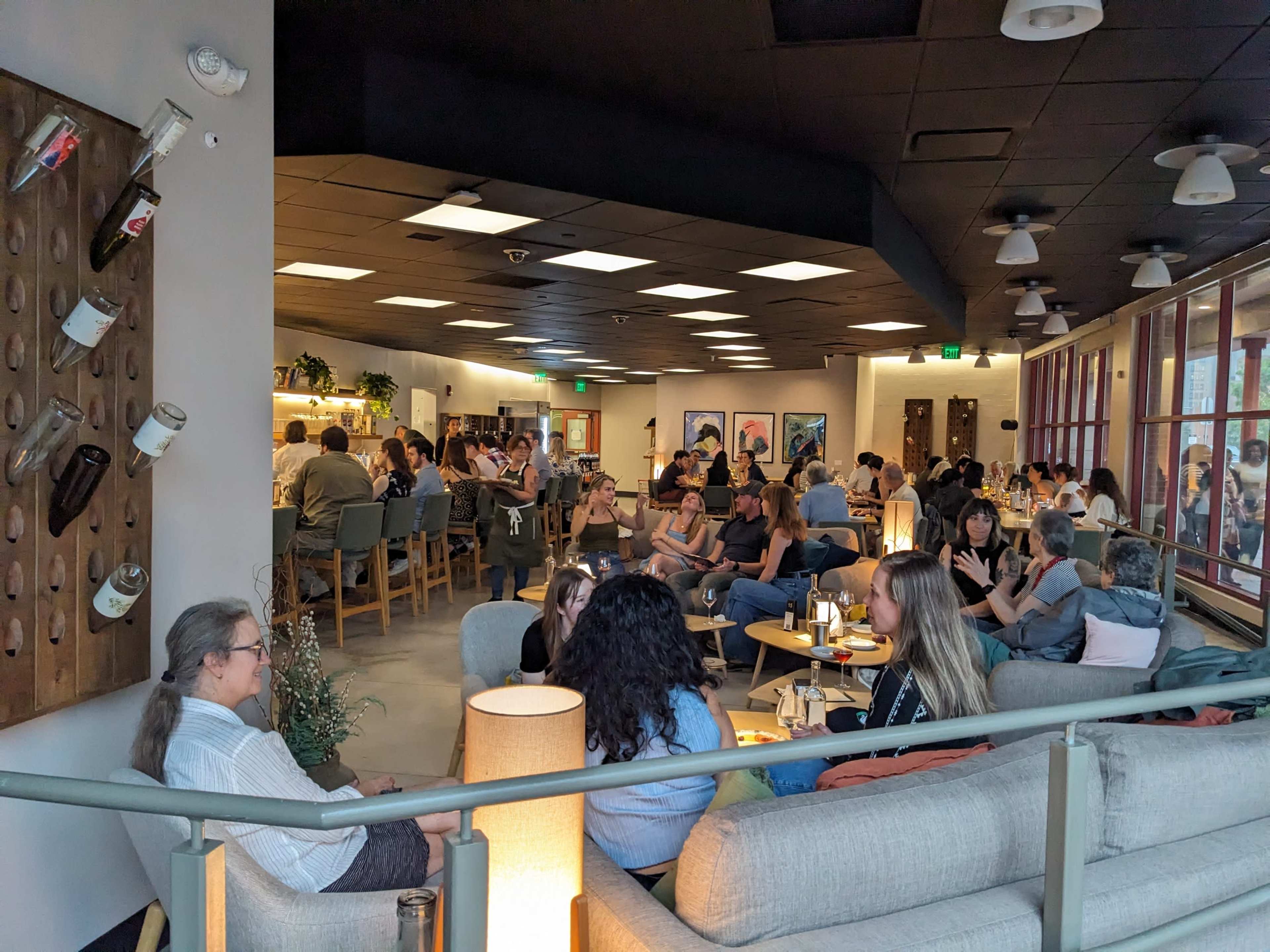 The image shows a crowded cafe interior with patrons seated at various tables engaged in conversation, while others are at the bar.