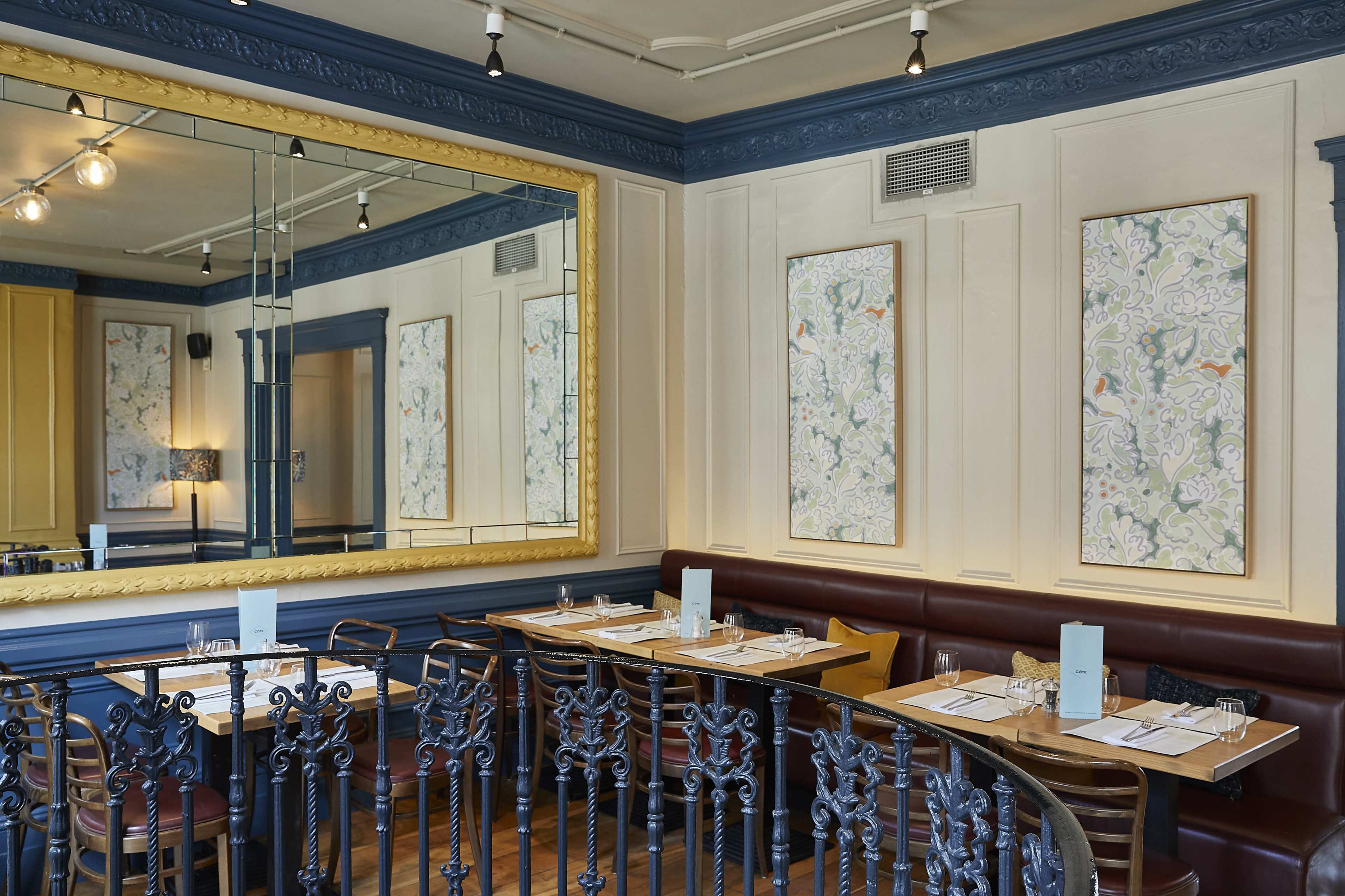 The image shows a stylish restaurant interior with a circular seating area, a large decorative mirror, and floral artwork on the walls.