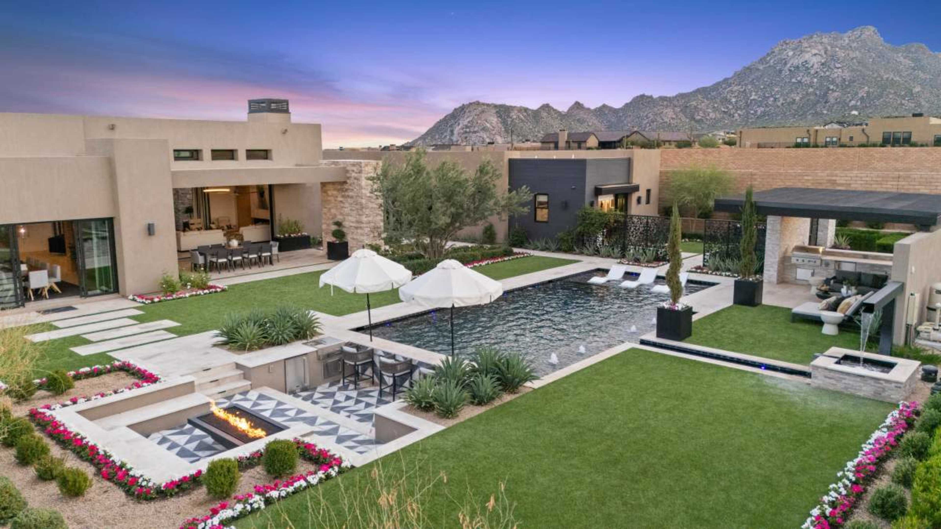 The image shows a modern home with a landscaped backyard featuring a swimming pool, lounge area, and surrounding mountains in the background.