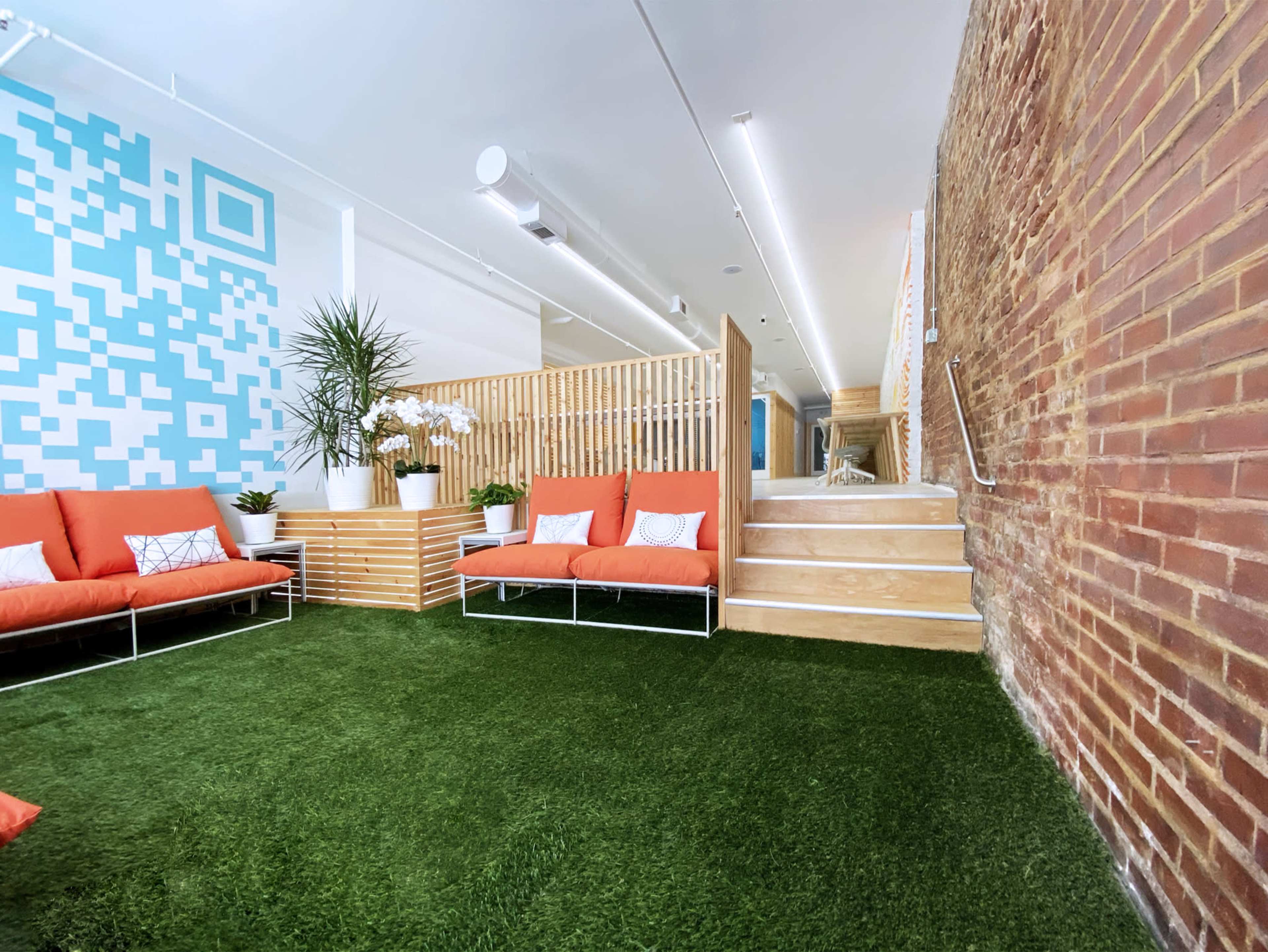 A modern interior space with orange couches, green artificial grass flooring, and a wooden partition separating different areas.