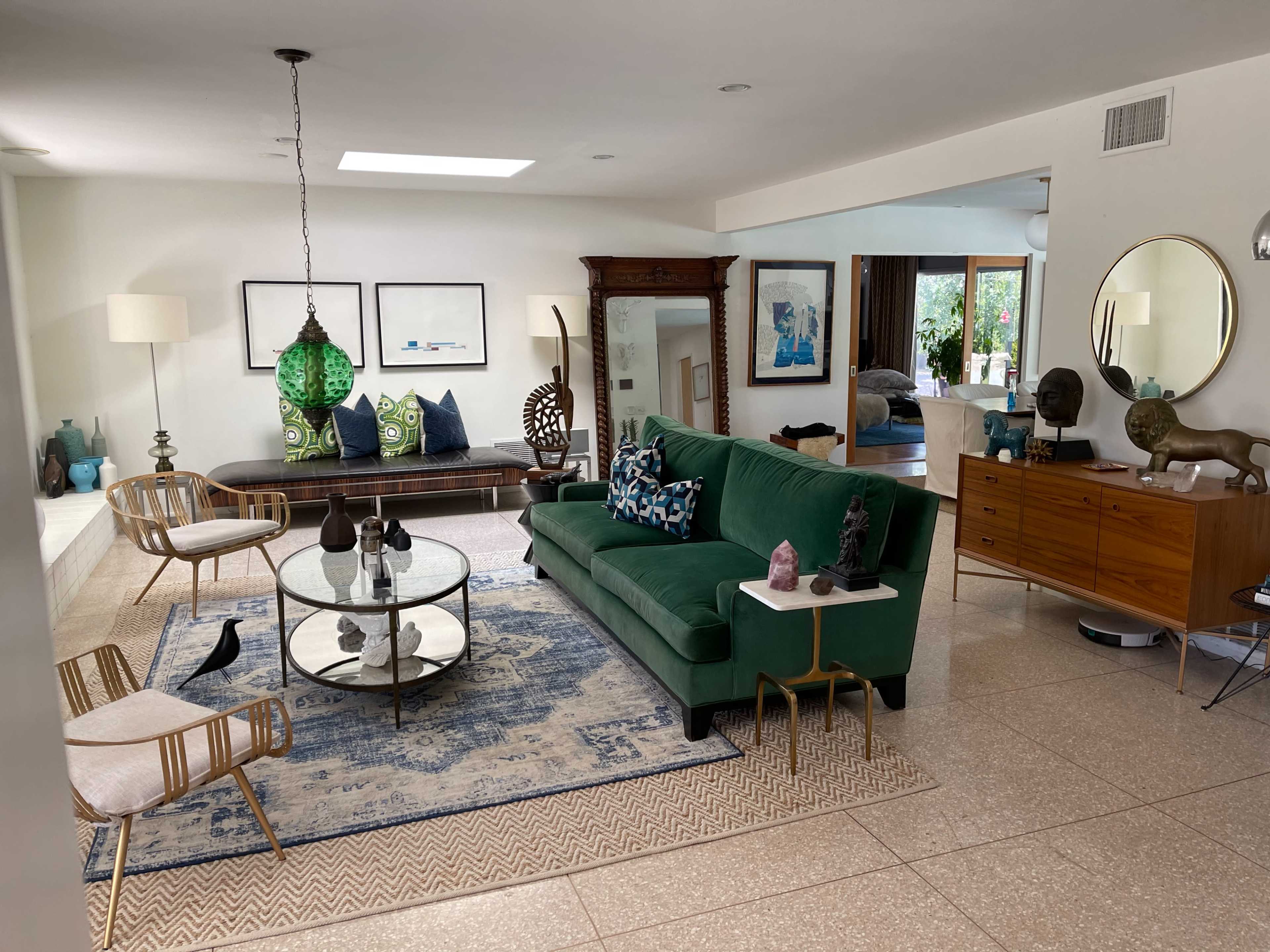 The image shows a spacious living room with a green sofa, glass coffee table, decorative furnishings, and an open layout connecting to other areas.