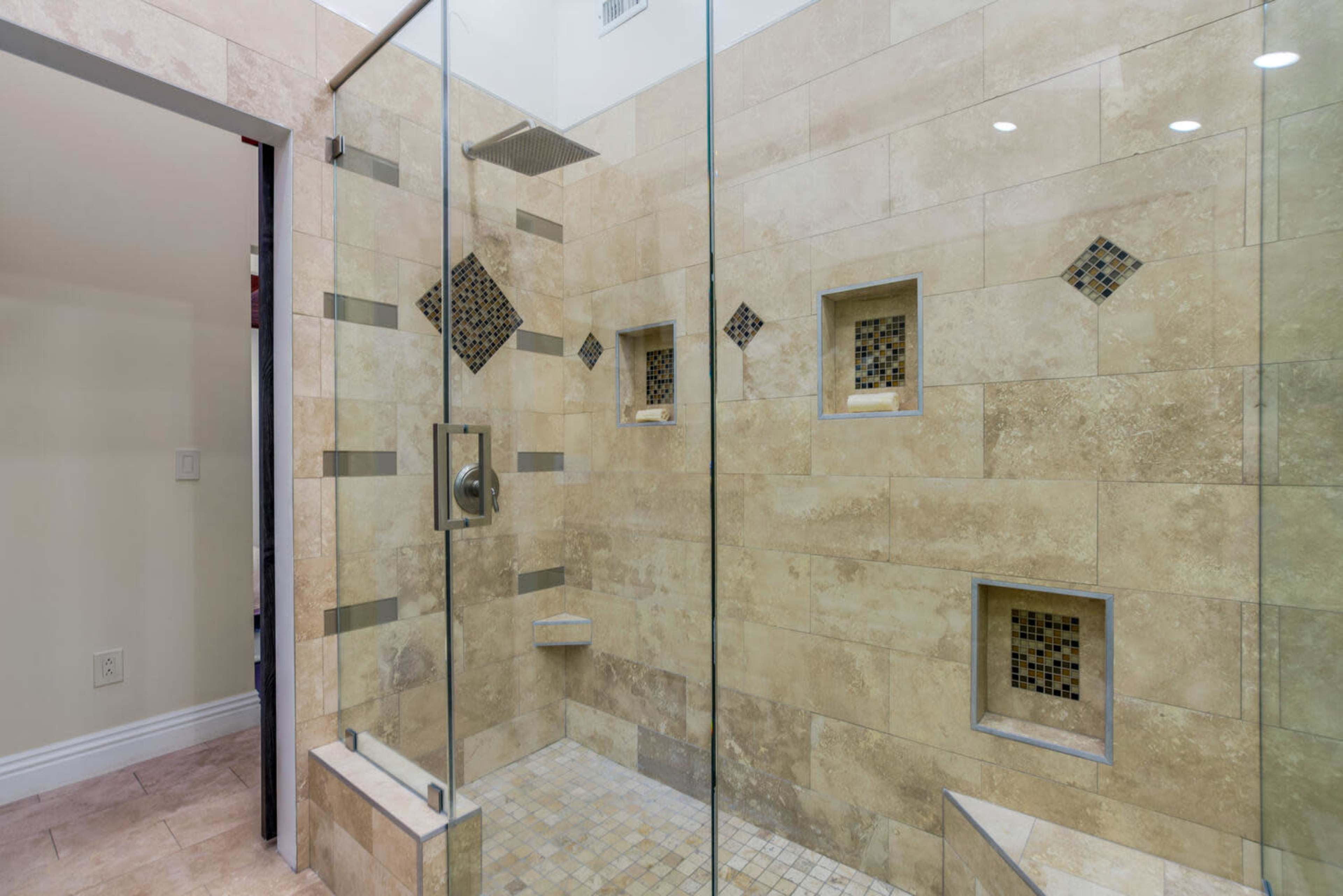 A glass-enclosed shower with stone tiles and recessed niches for toiletries.