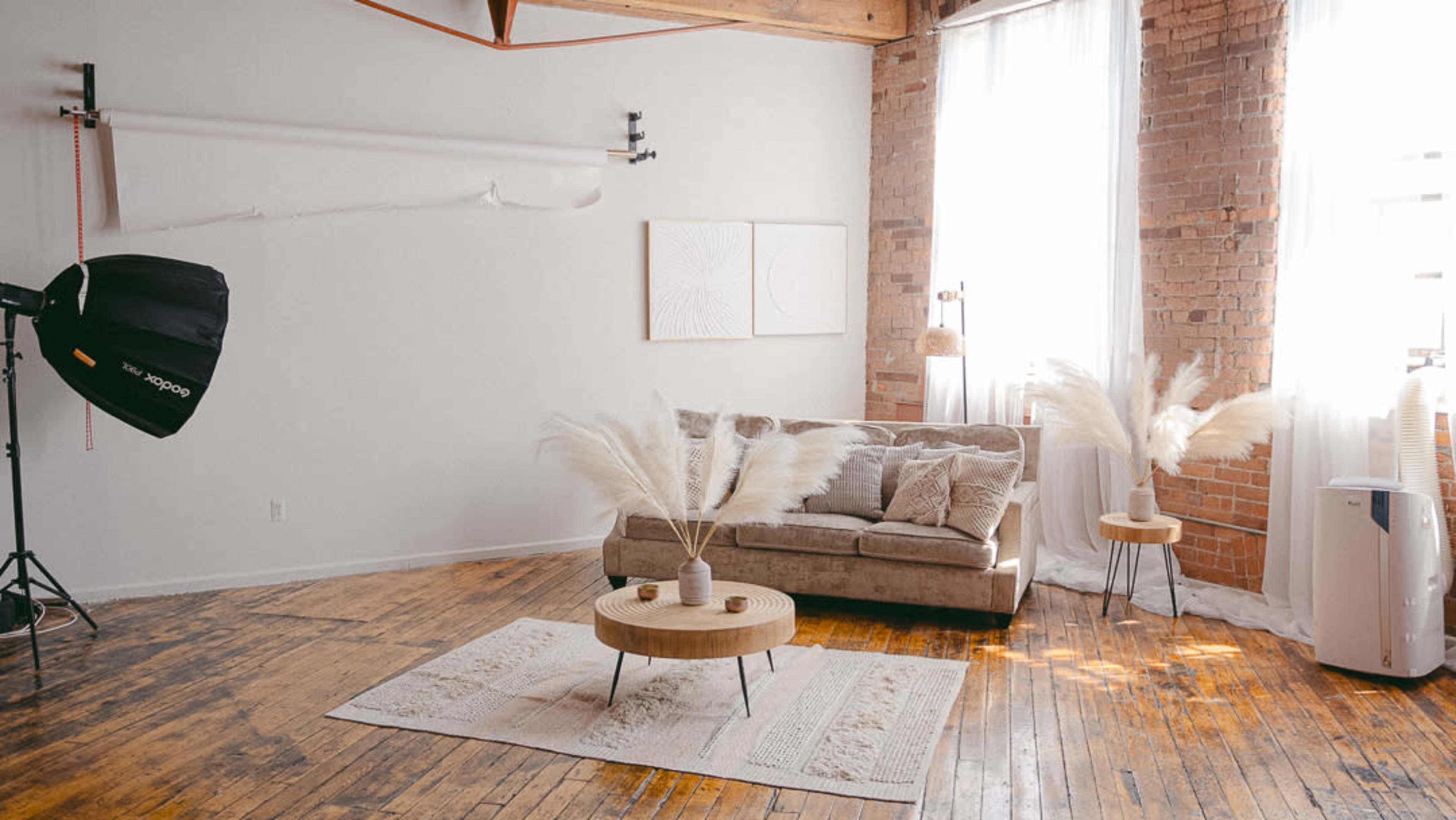 A light-filled room featuring a beige couch, two side tables with decorative plants, and a large soft area rug on a wooden floor.