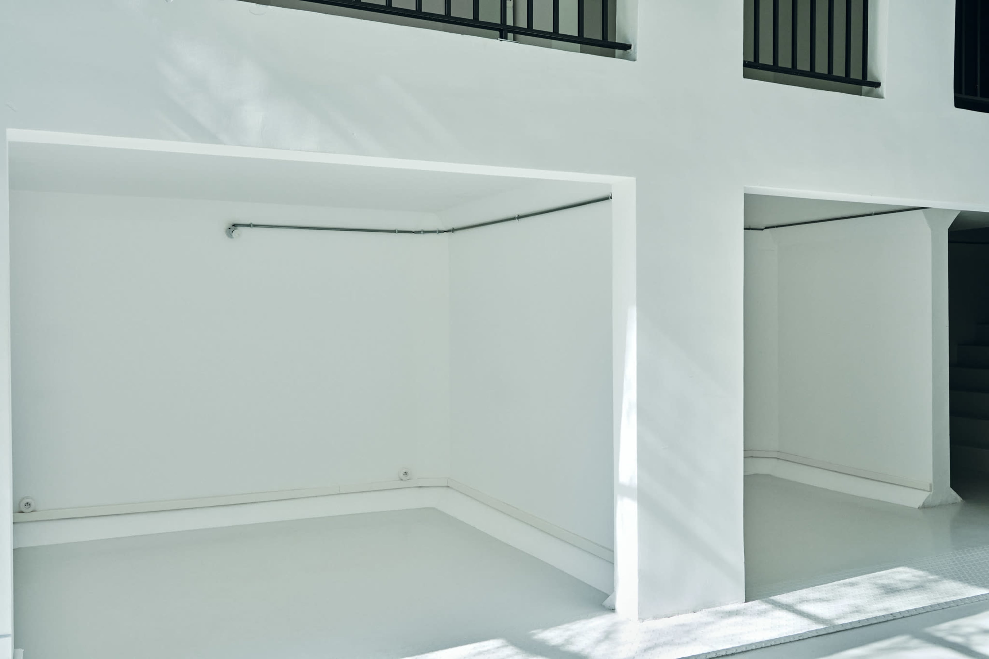 The image shows a spacious, brightly lit area with white walls and floors, featuring two recessed sections with minimalist design.