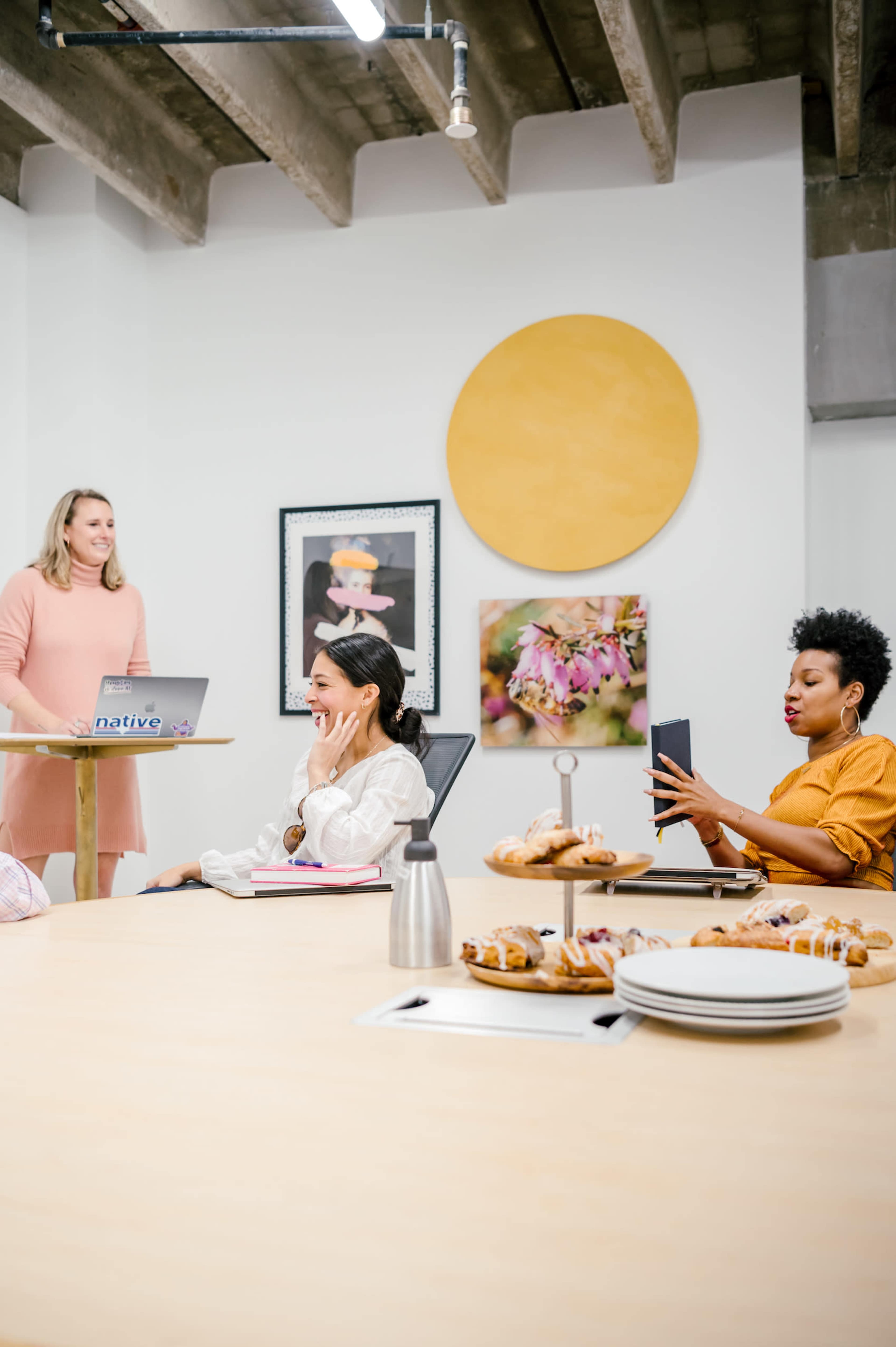 A group of people is gathered in a conference room with food on the table while one person presents at the front.