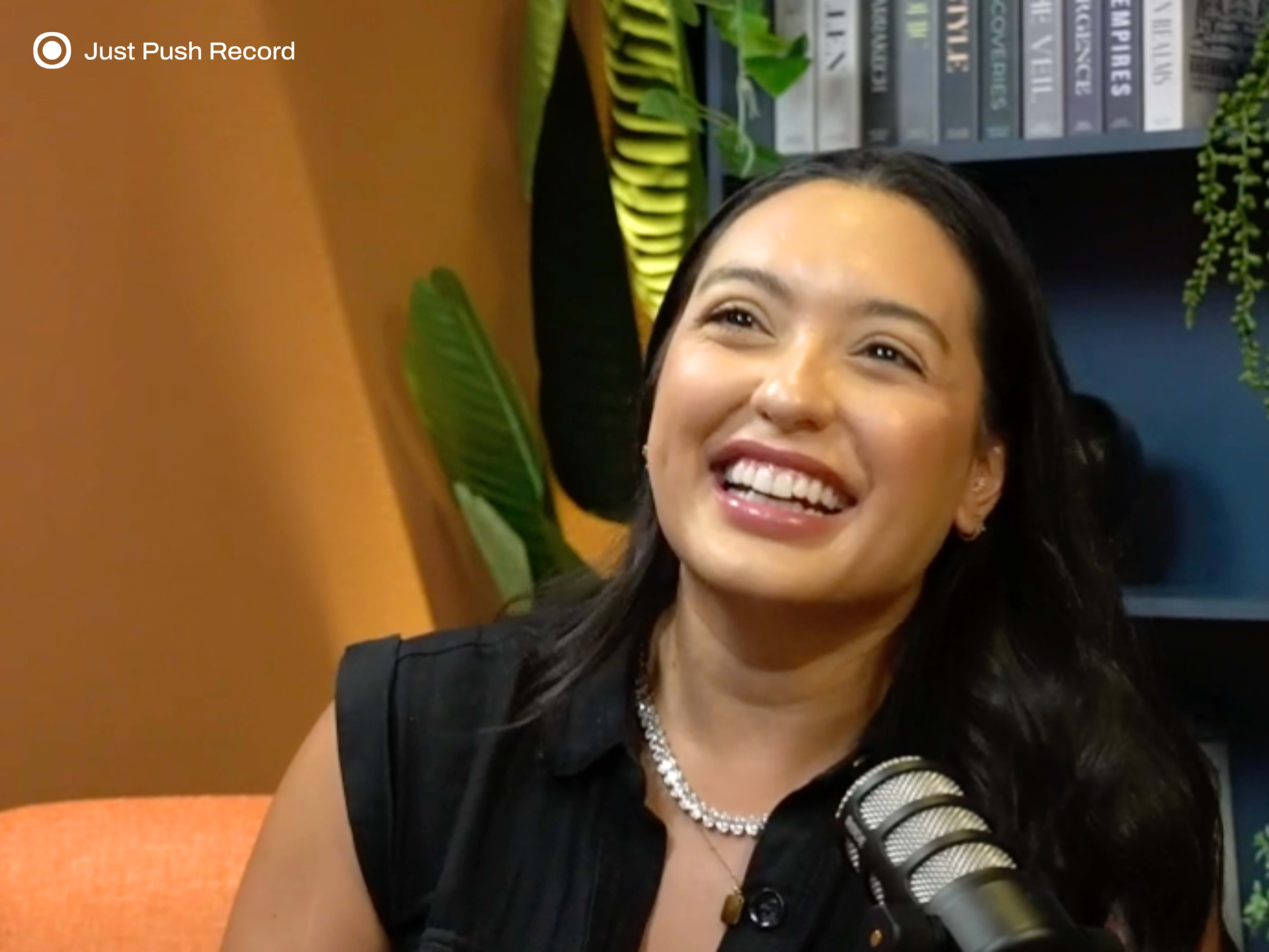 A woman is sitting in a brightly colored room, smiling and speaking into a microphone.