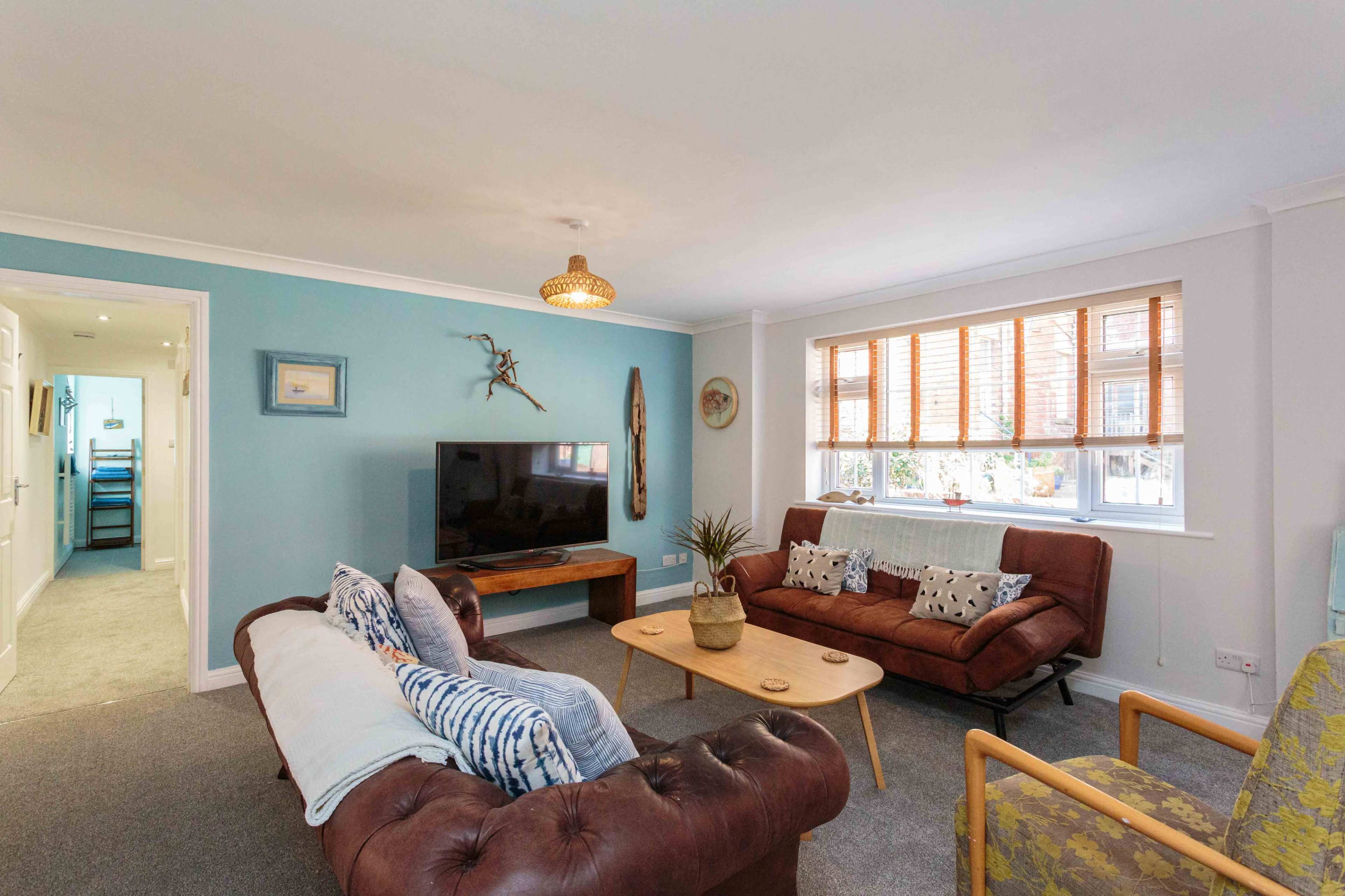 A modern living room features a television, a wooden coffee table, brown leather sofas, and a decorative wall.