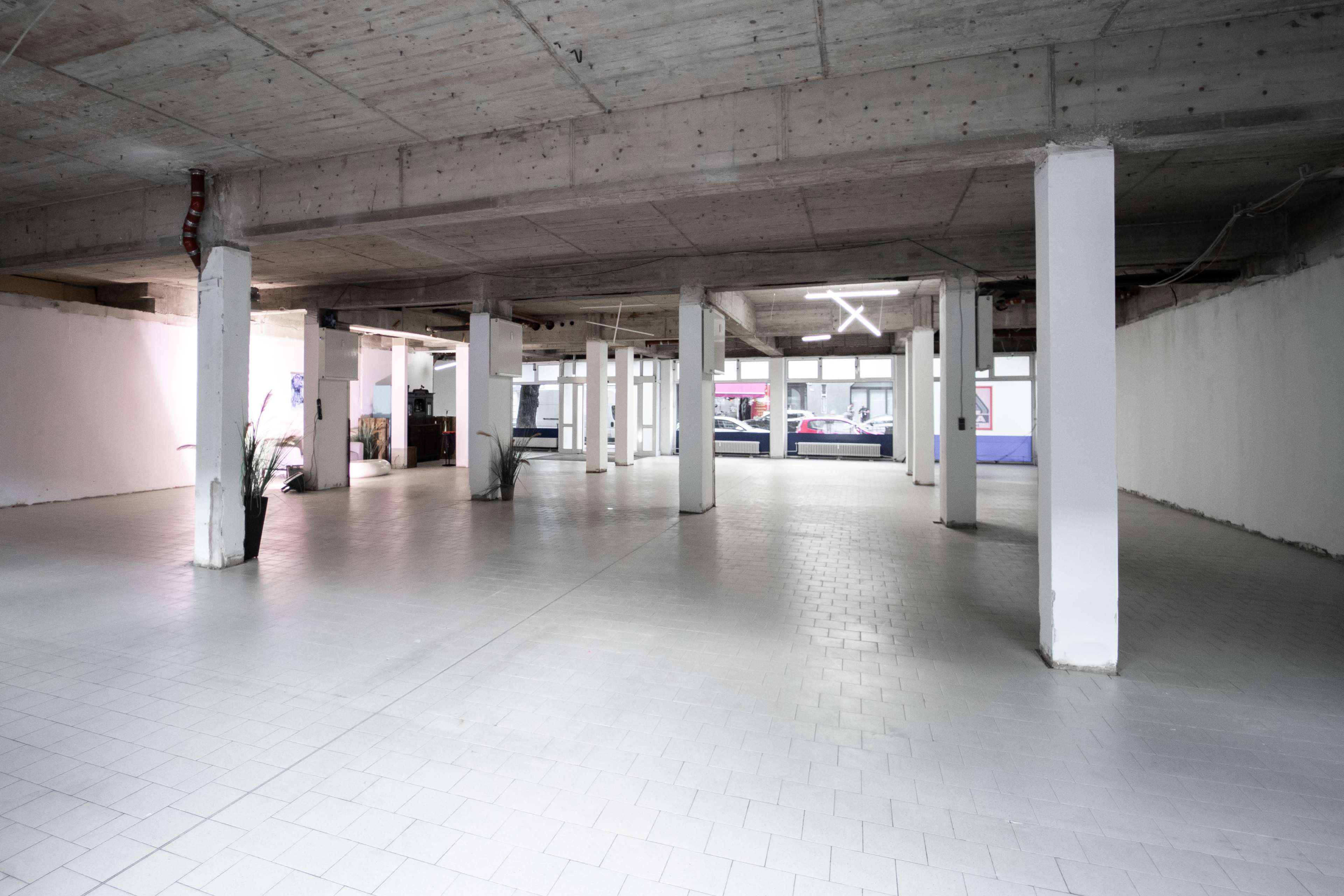 A spacious, empty interior of a building with concrete pillars and a white tiled floor.