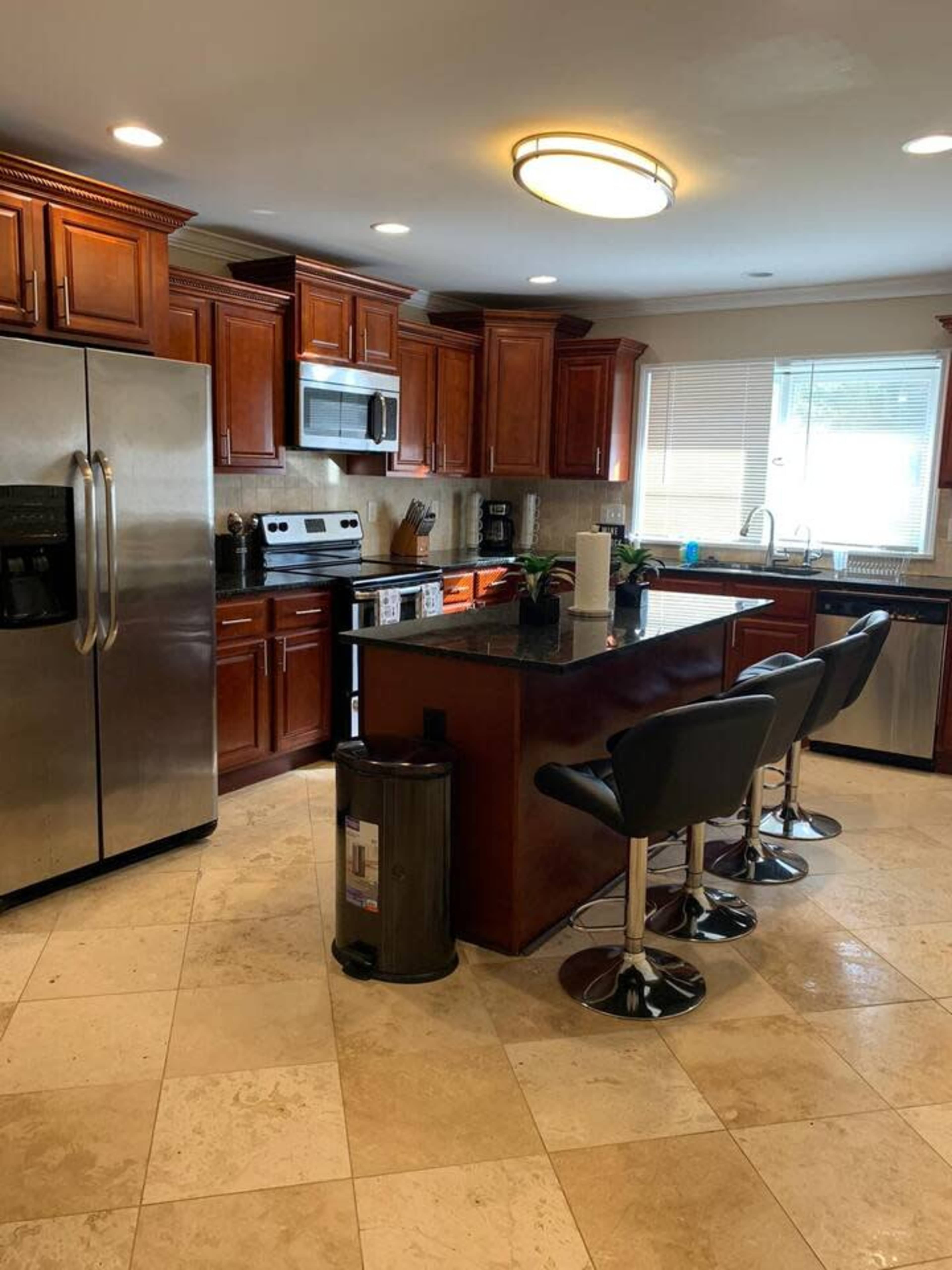 The kitchen features wooden cabinets, stainless steel appliances, a granite countertop, and two bar stools at the island.