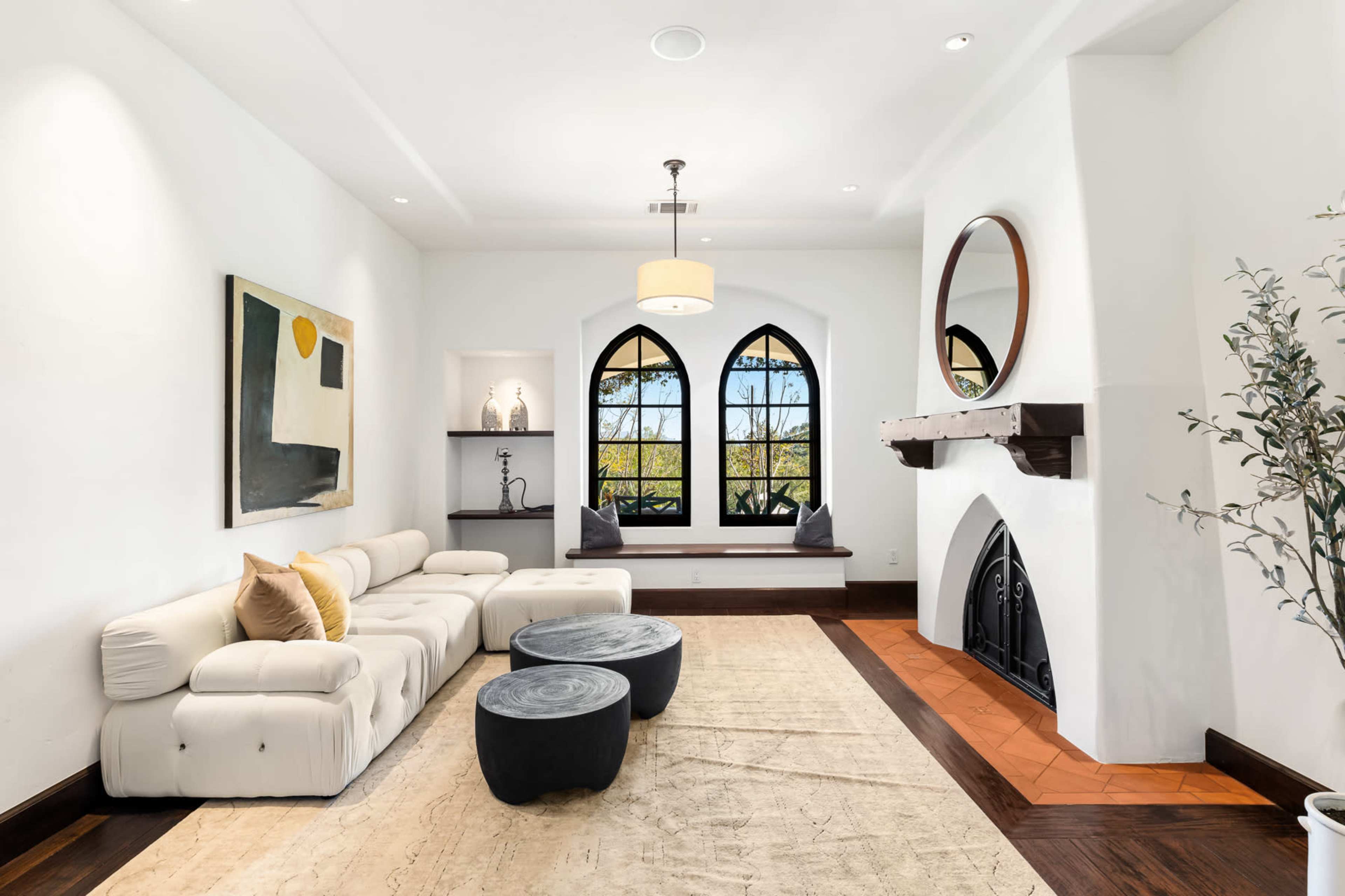 A spacious living room features a white sectional sofa, two round black coffee tables, and large arched windows with built-in seating.