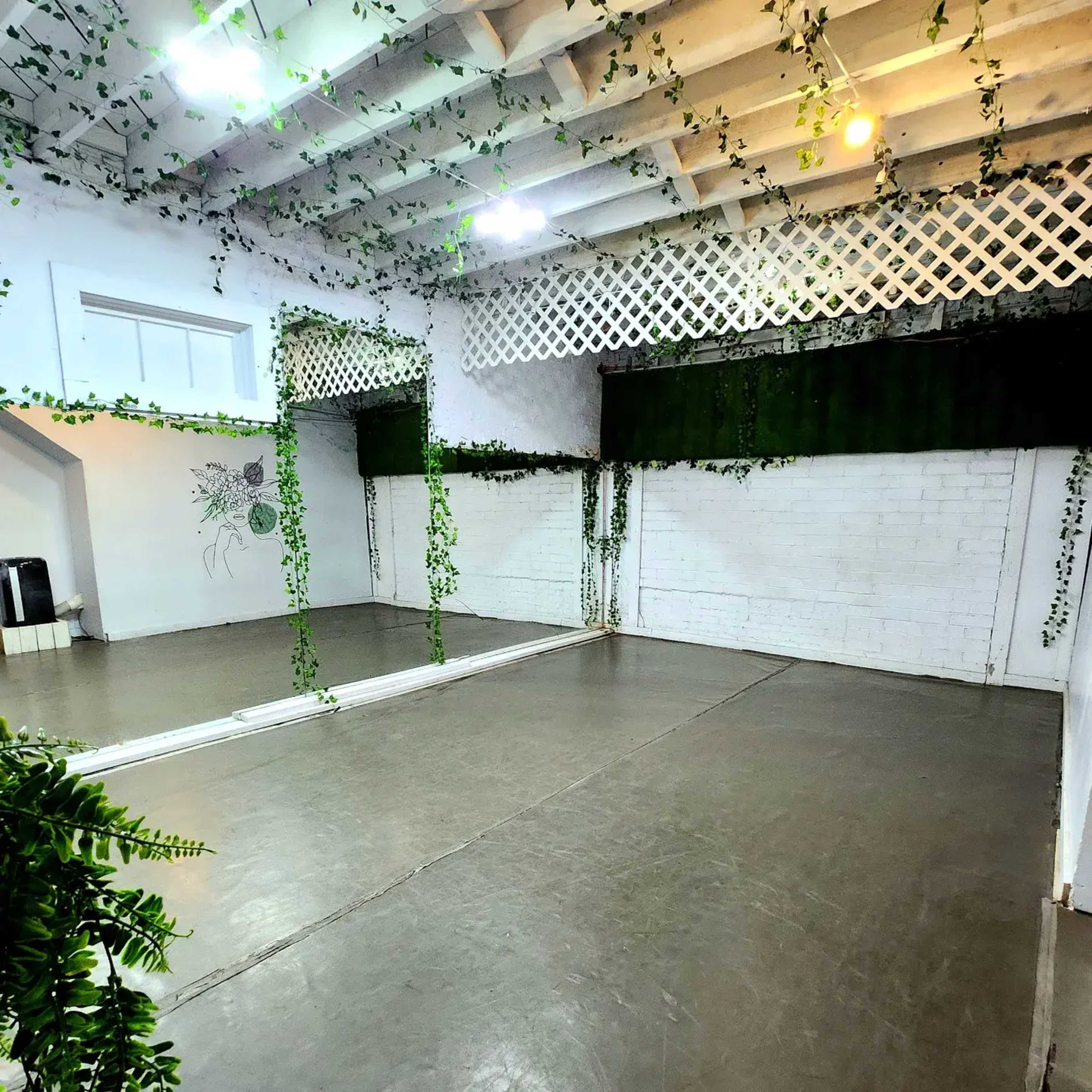 A spacious room with a polished concrete floor, exposed wooden beams, and green vines draping from the ceiling and walls.
