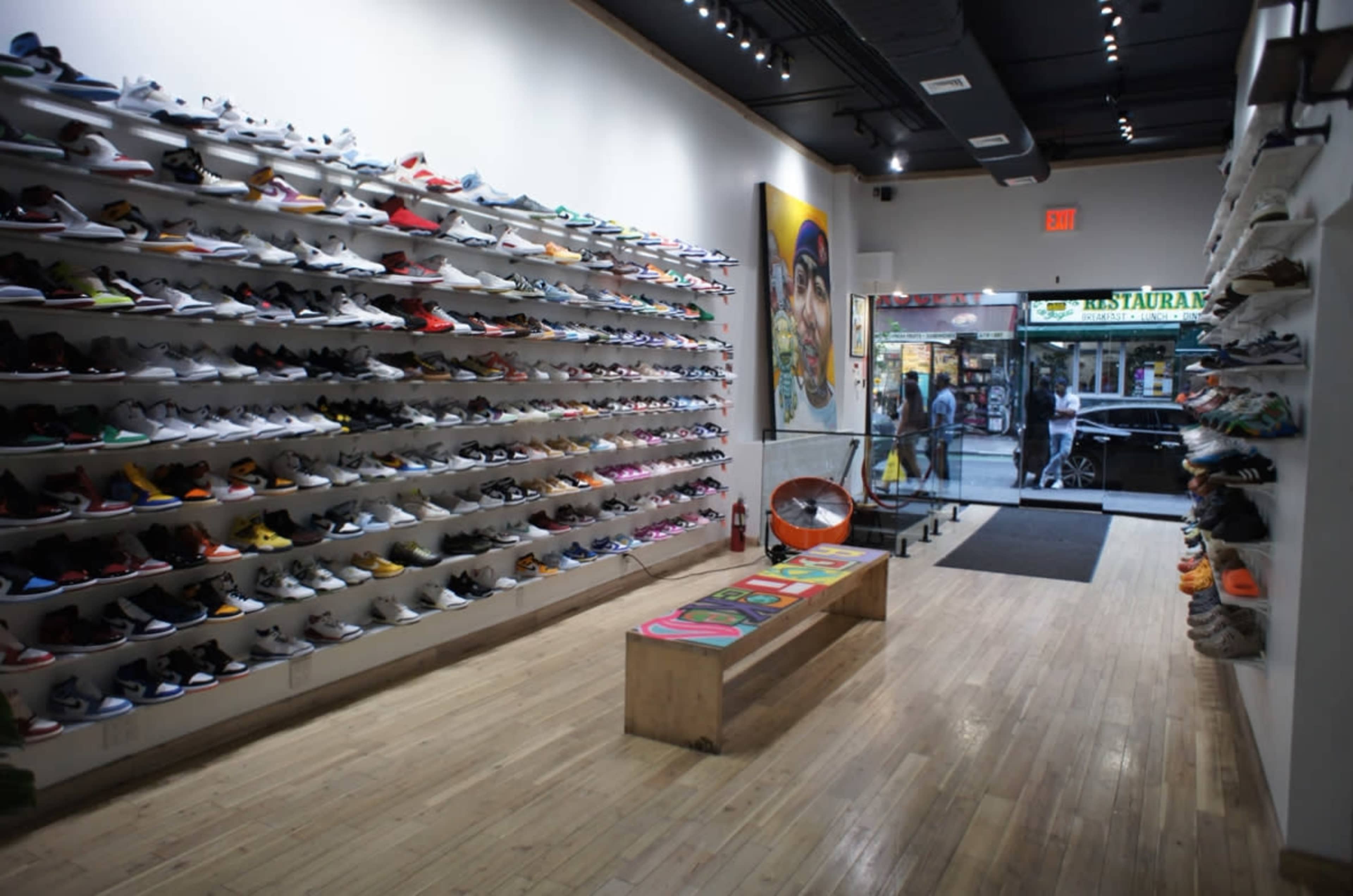 An interior of a shoe store with rows of colorful sneakers displayed on the walls and a wooden bench in the center.