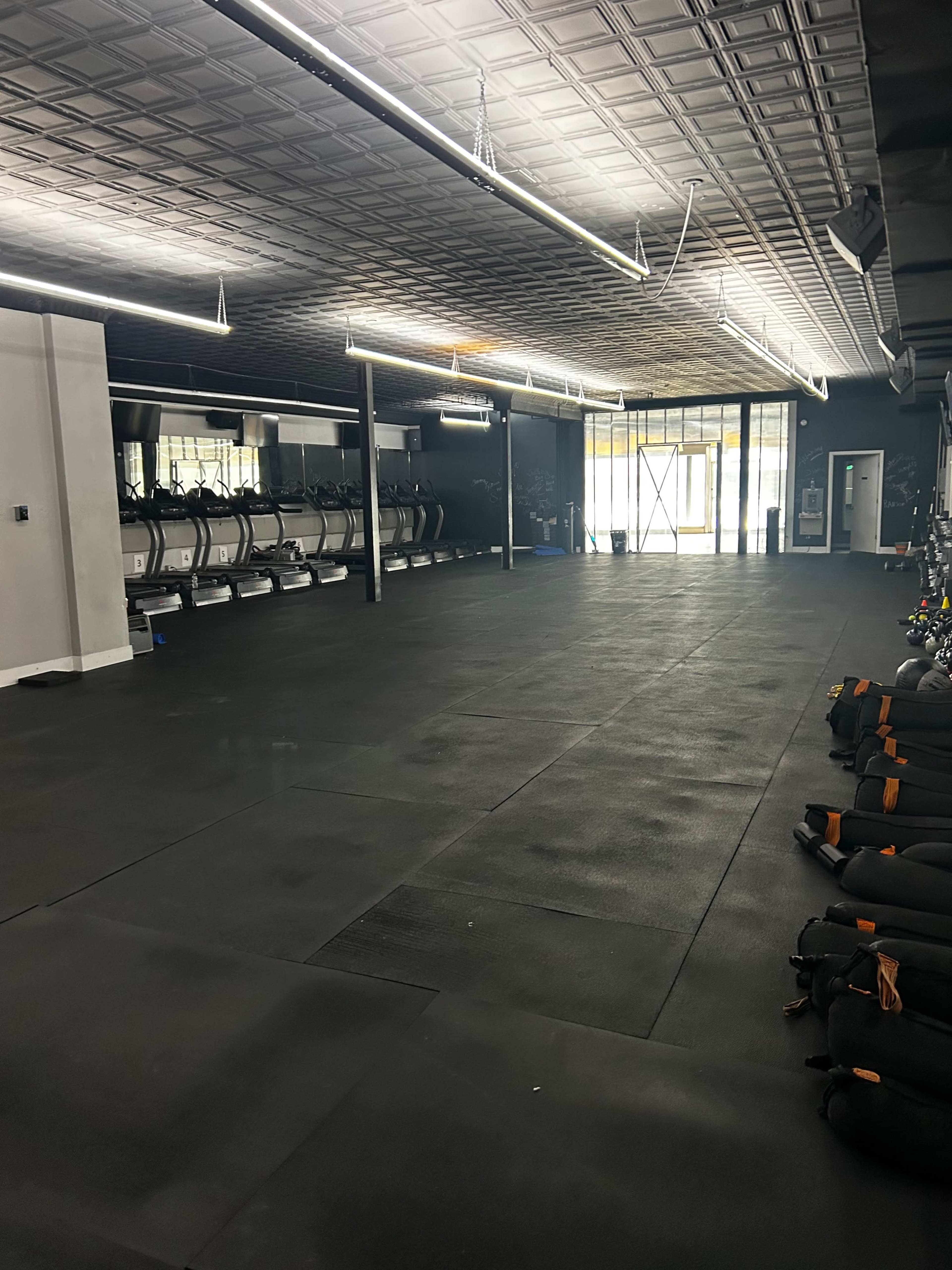 The image shows an empty gym space with rows of treadmills along one wall and exercise equipment organized on the right side.