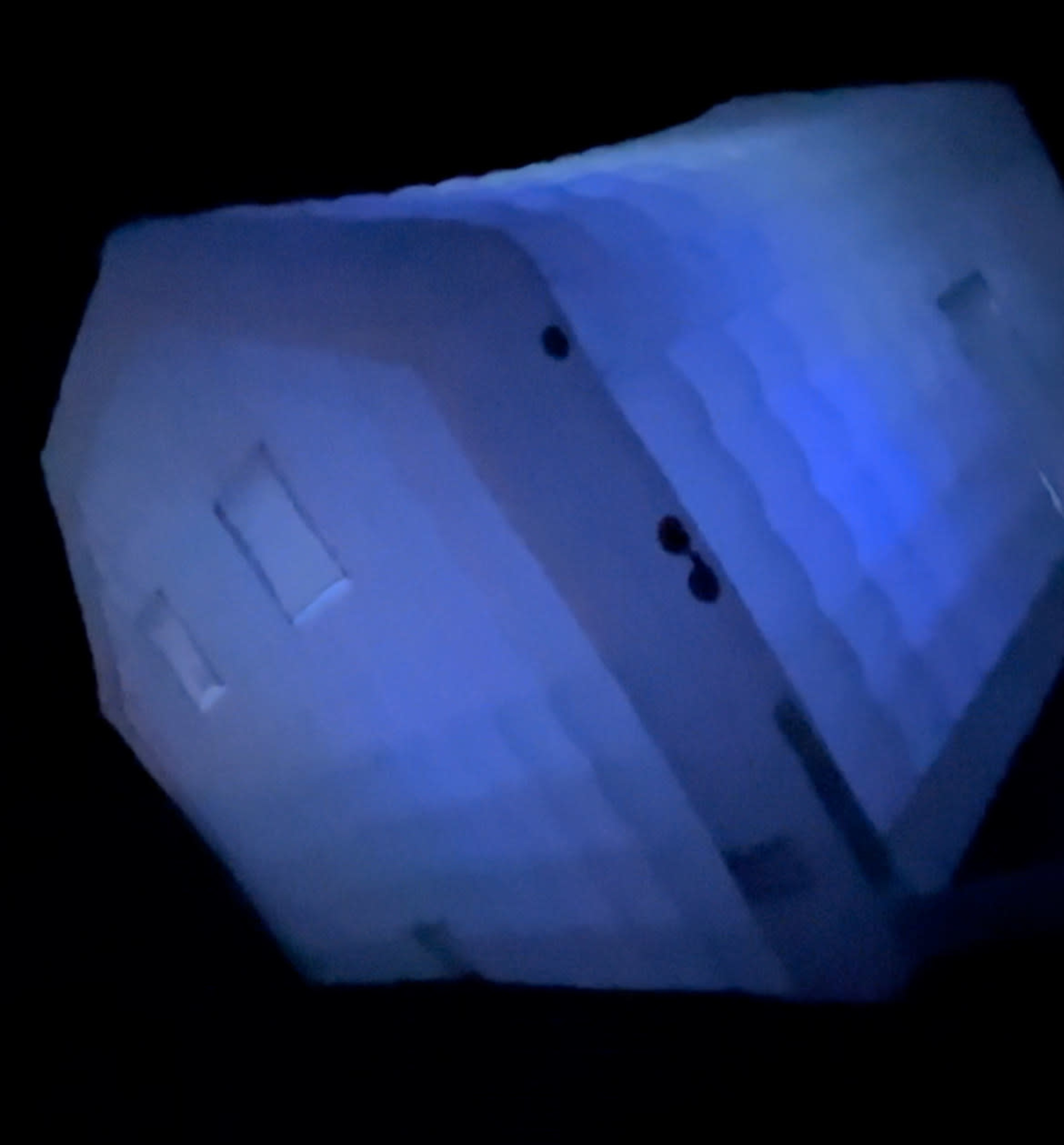 A white, inflated structure with small windows is illuminated by a blue light against a dark background.