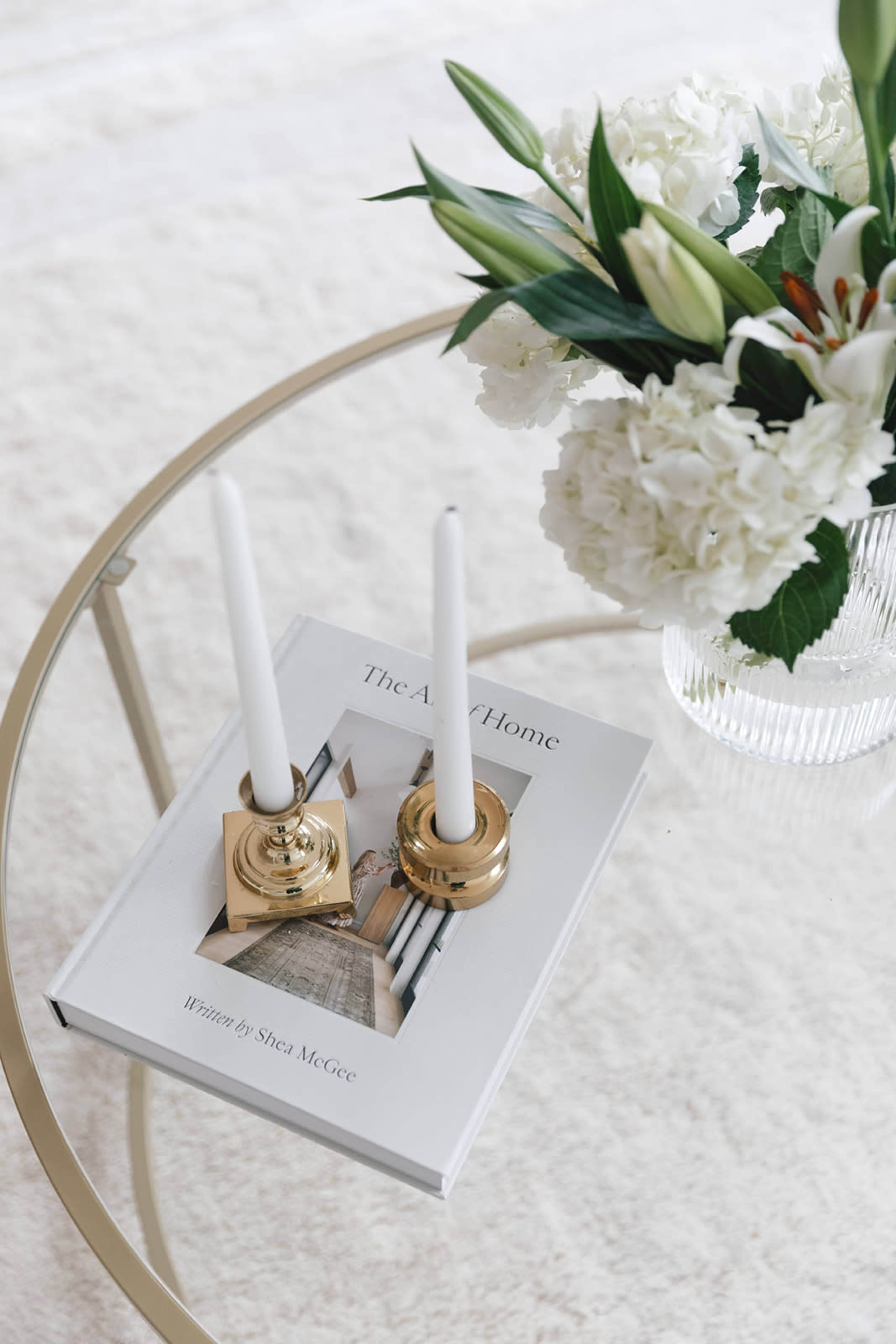 A coffee table displays a book titled "The Art of Home" along with two white candles in gold holders and a vase of flowers.