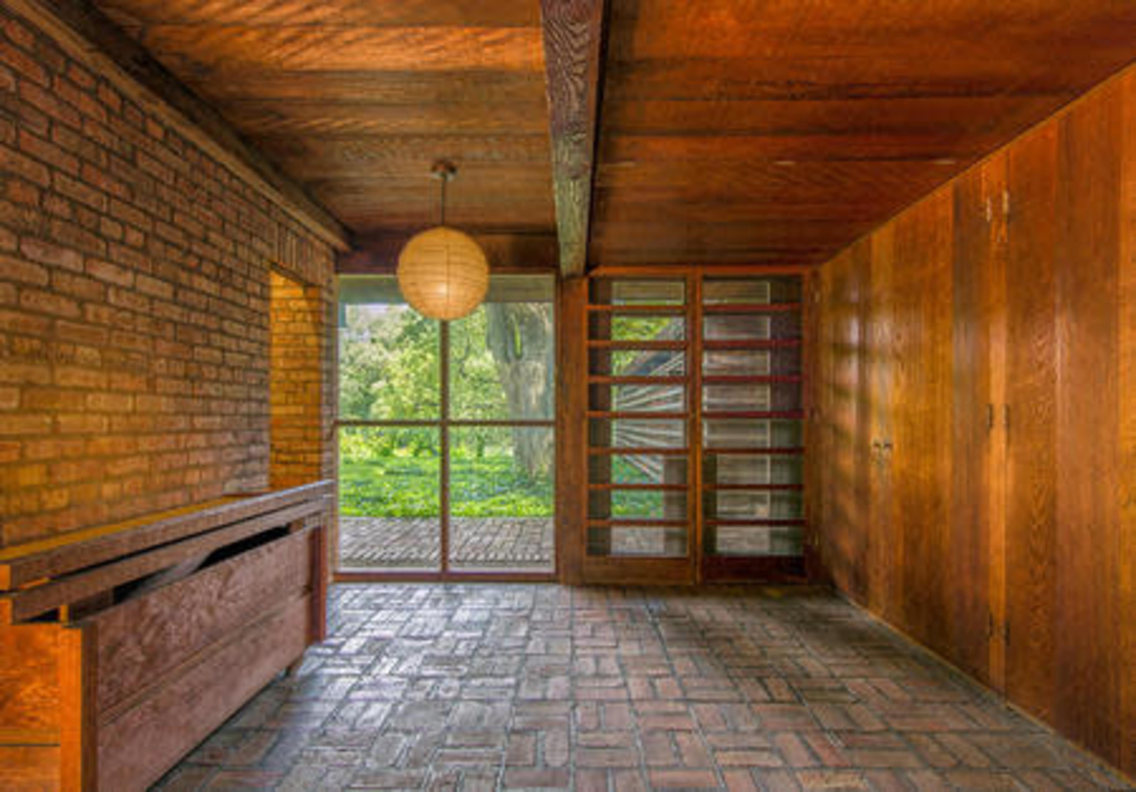 The image shows a spacious interior with brick walls, wooden beams, and large windows overlooking a green landscape.