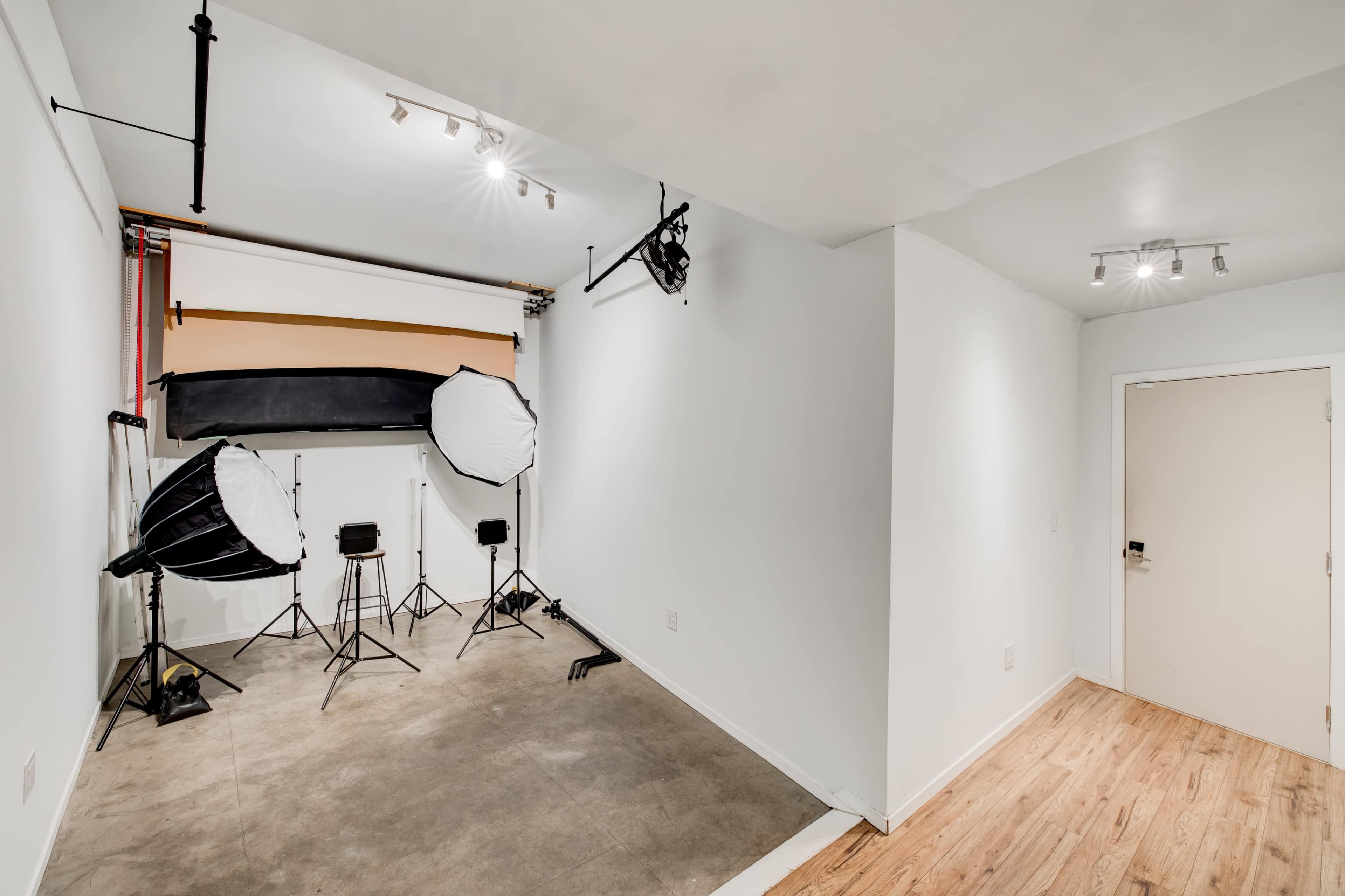 A photography studio with two large softbox lights, a backdrop setup, and a wooden door leading to an adjacent room.