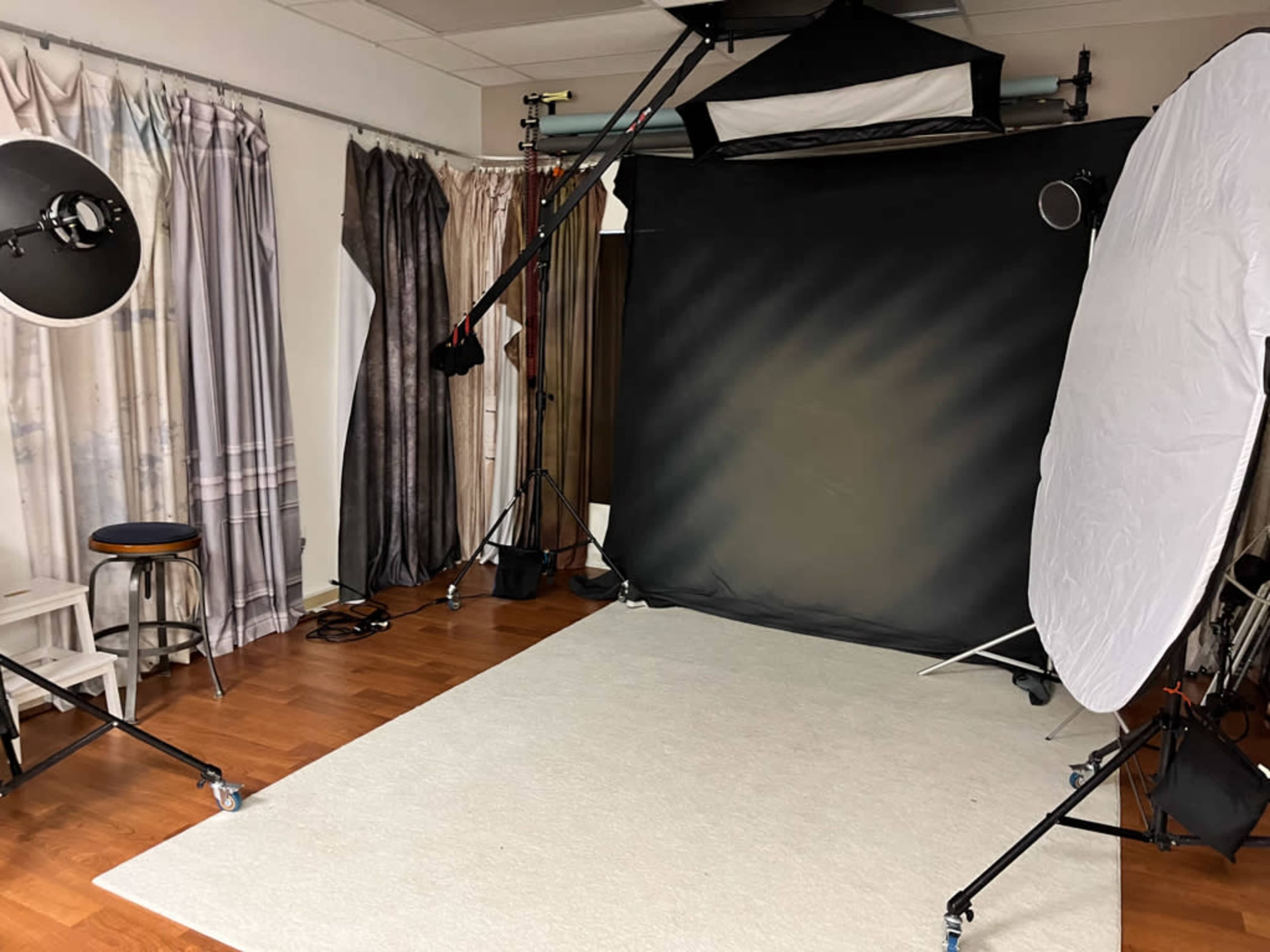 A photography studio with a black backdrop, softbox lighting, and seating arranged on a wooden floor.