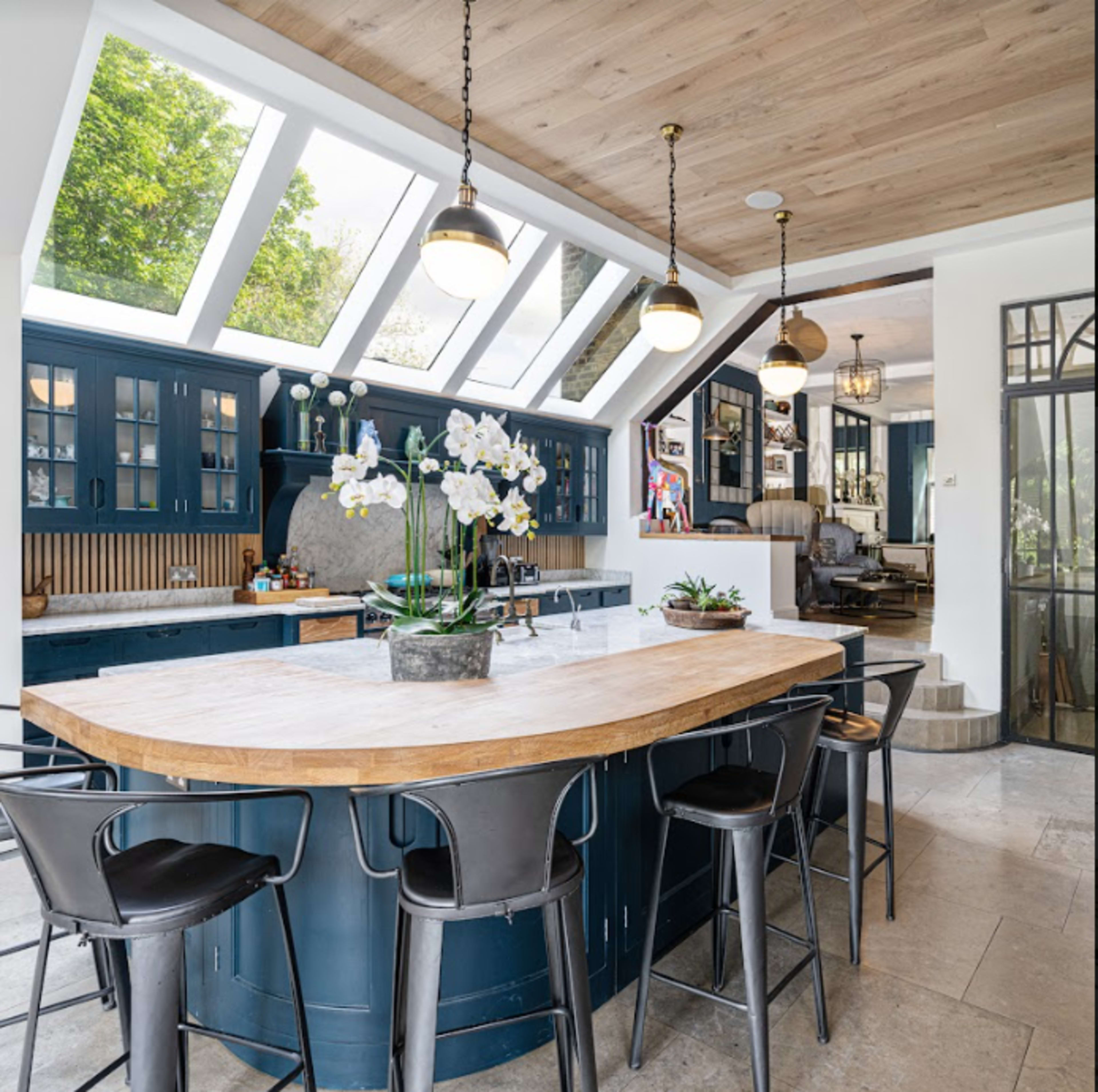 A modern kitchen with a large wooden island, blue cabinetry, and skylights allowing natural light to fill the space.