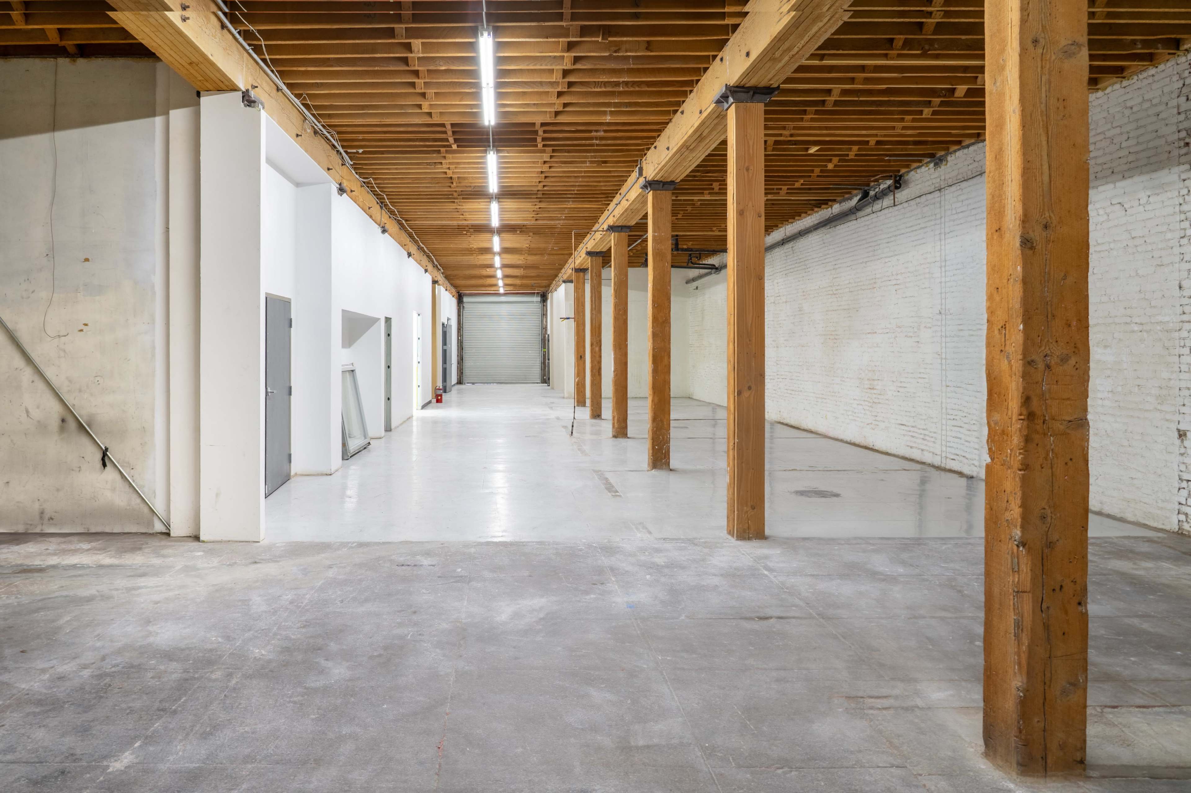 The image shows an empty warehouse space with wooden support beams and concrete flooring.