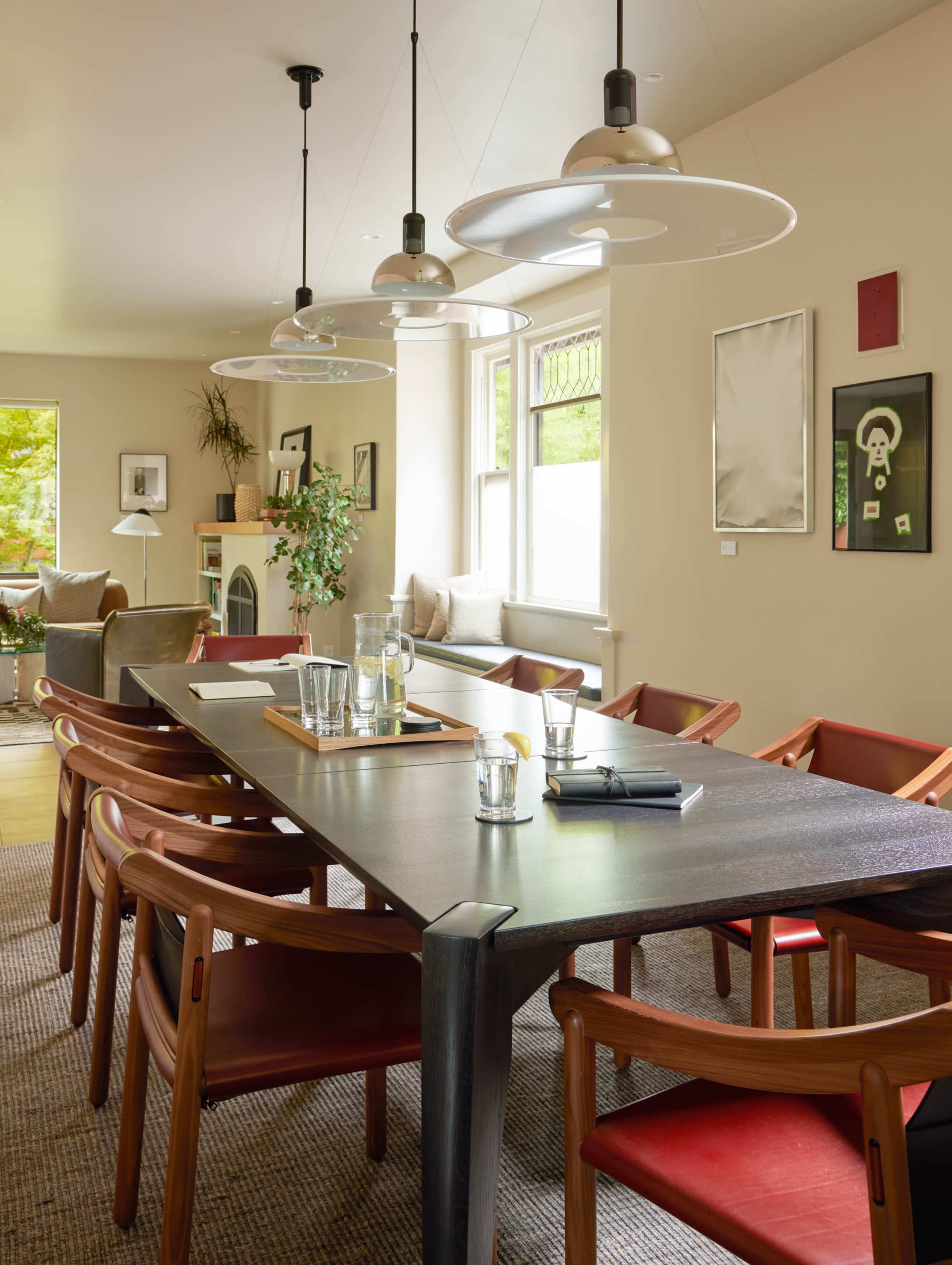 A modern conference room features a long wooden table surrounded by chairs, with large pendant lights hanging overhead and artwork on the walls.