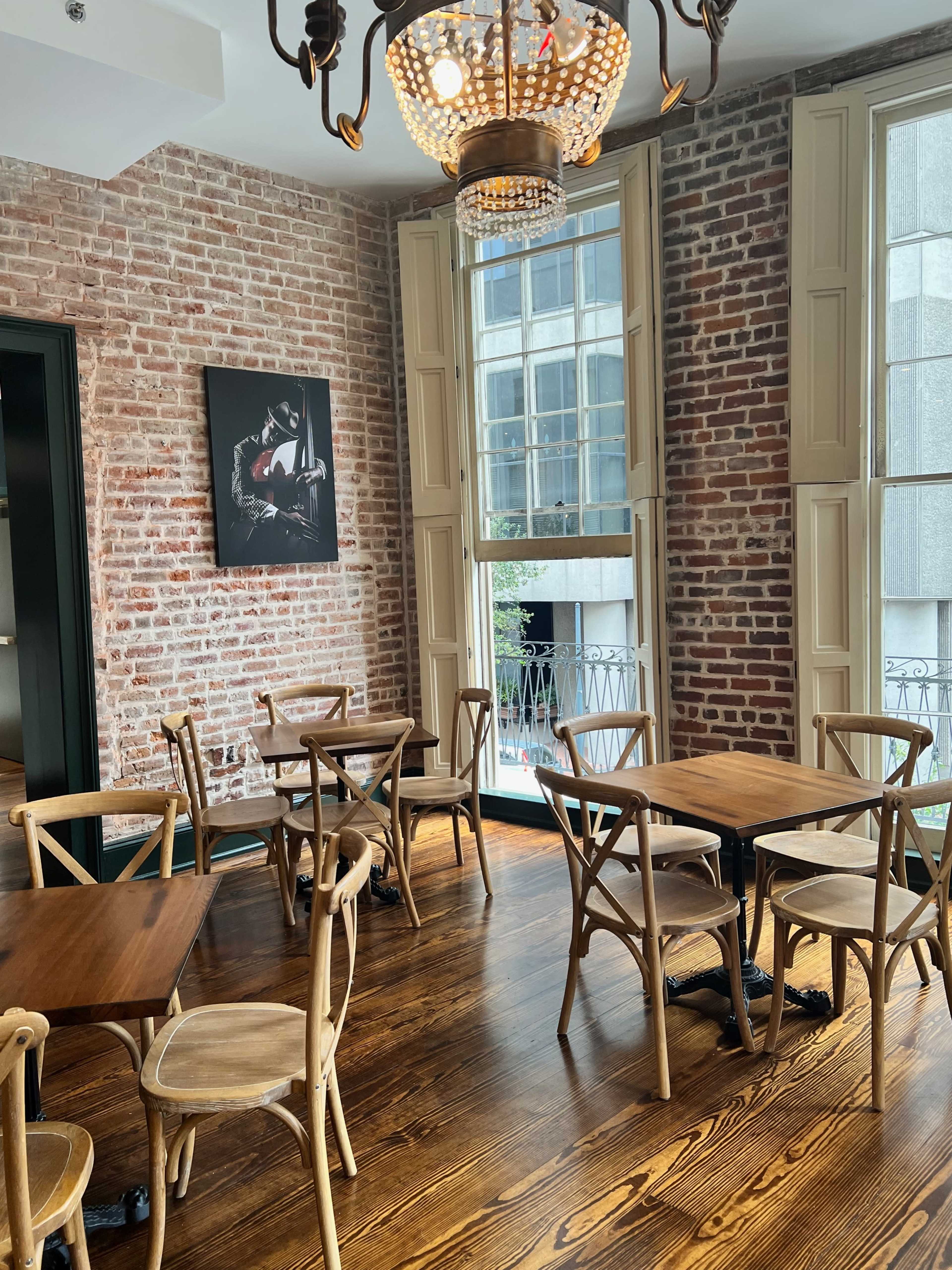 A room featuring wooden tables and chairs, exposed brick walls, and large windows with natural light.