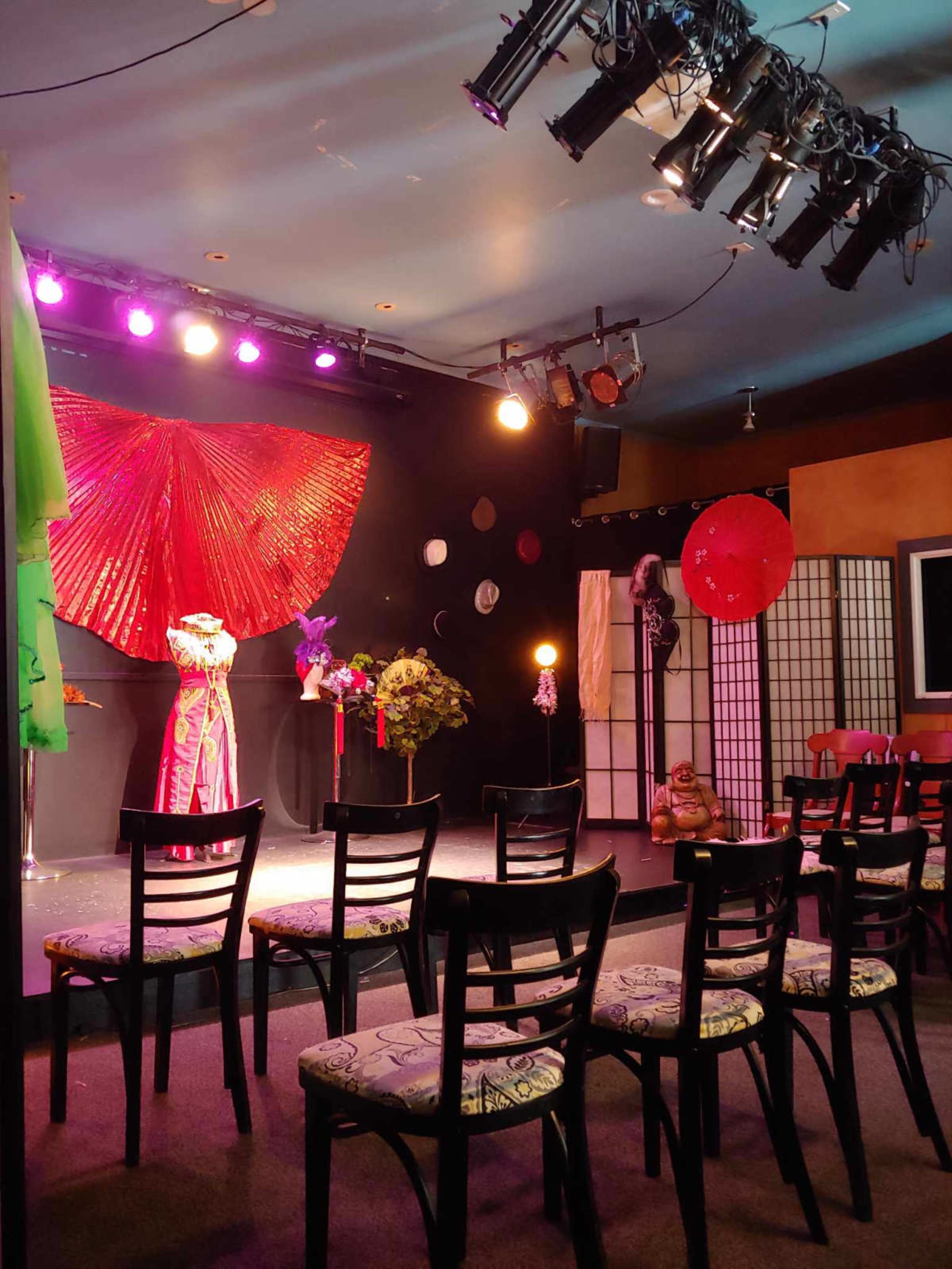 A stage set up for a performance, featuring a red backdrop, colorful costumes, and an arrangement of chairs for an audience.