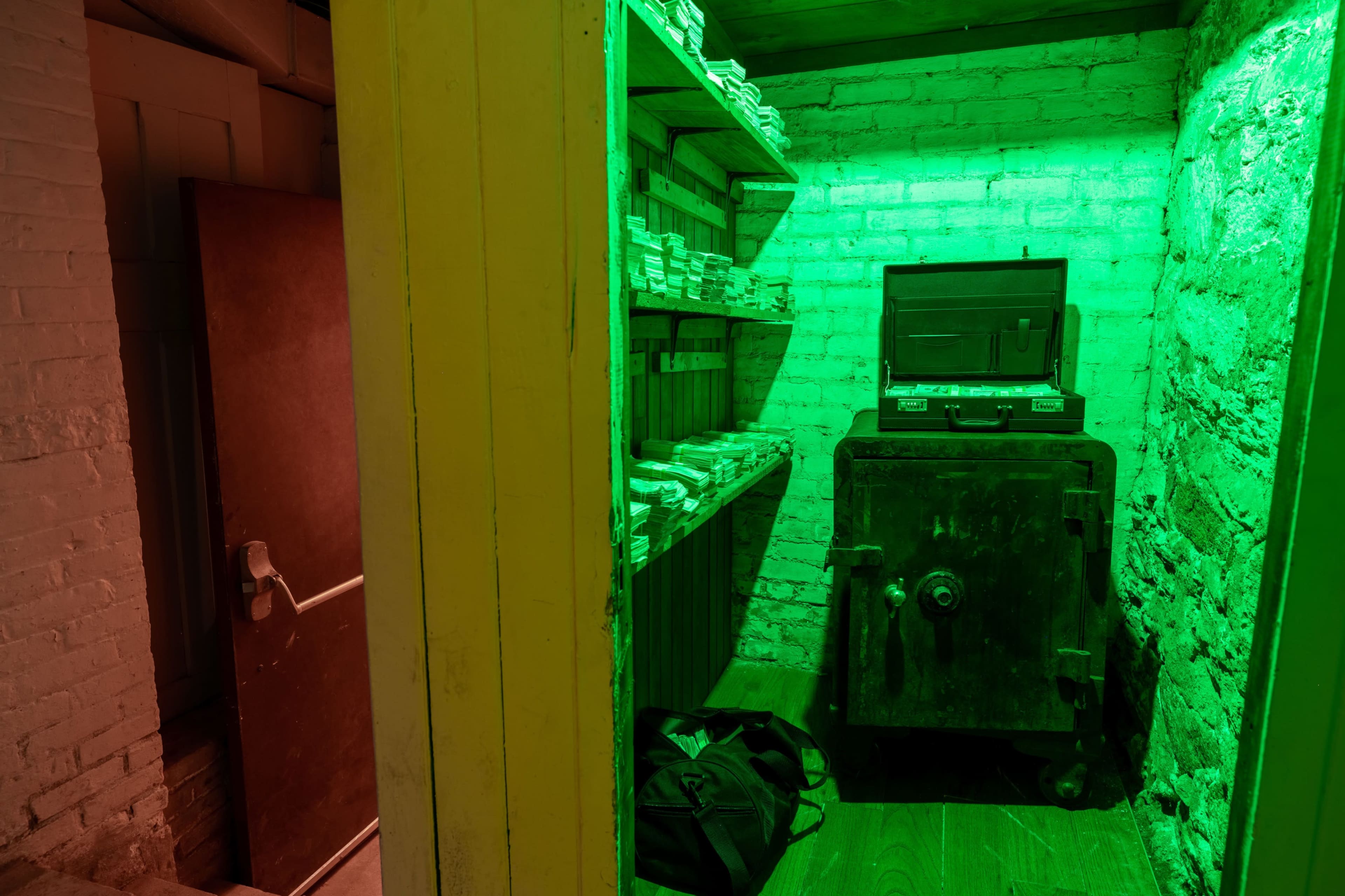 A small room with green lighting, featuring shelves lined with stacks of paper and an old safe against the wall.